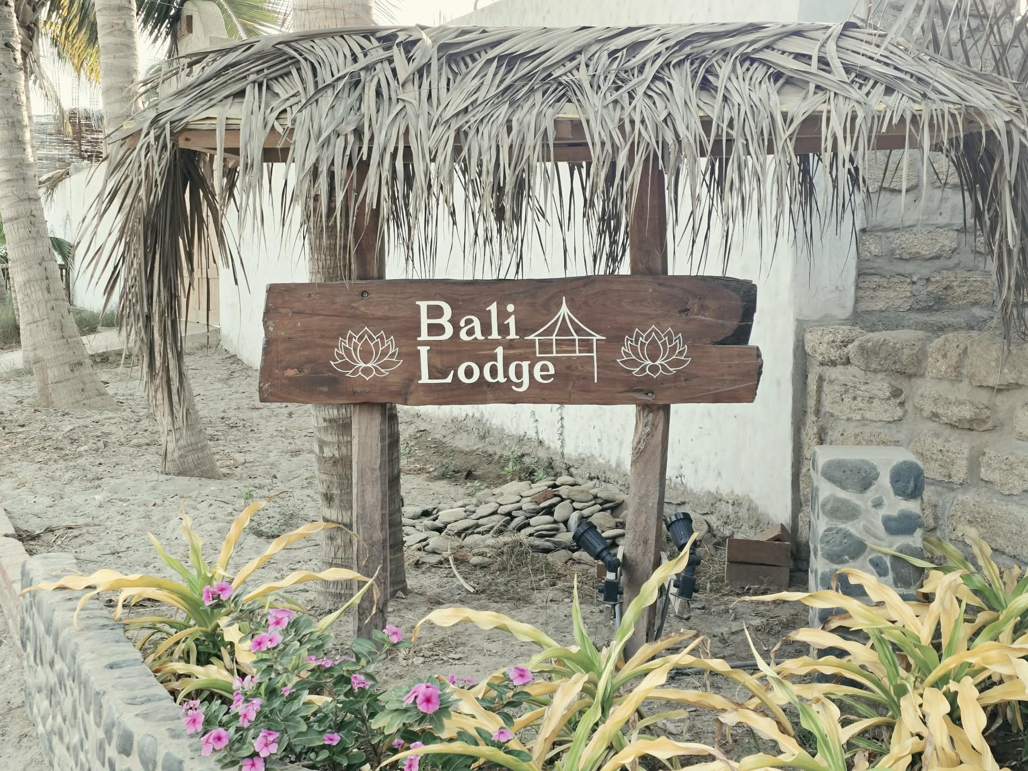 Handcrafted wooden Bali Lodge entrance sign with carved lotus flowers sheltered under a palapa thatch roof