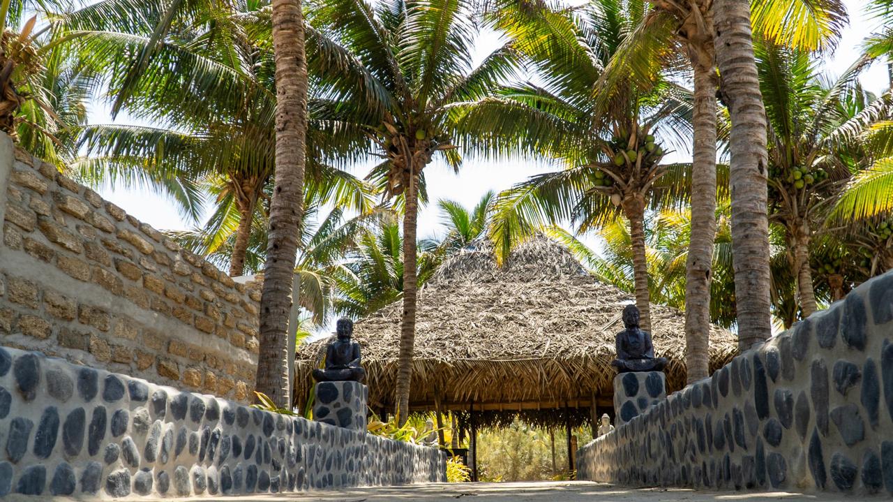 Stone Buddhas and coconut palms leading to the palapa-thatched reception pavilion at Bali Lodge