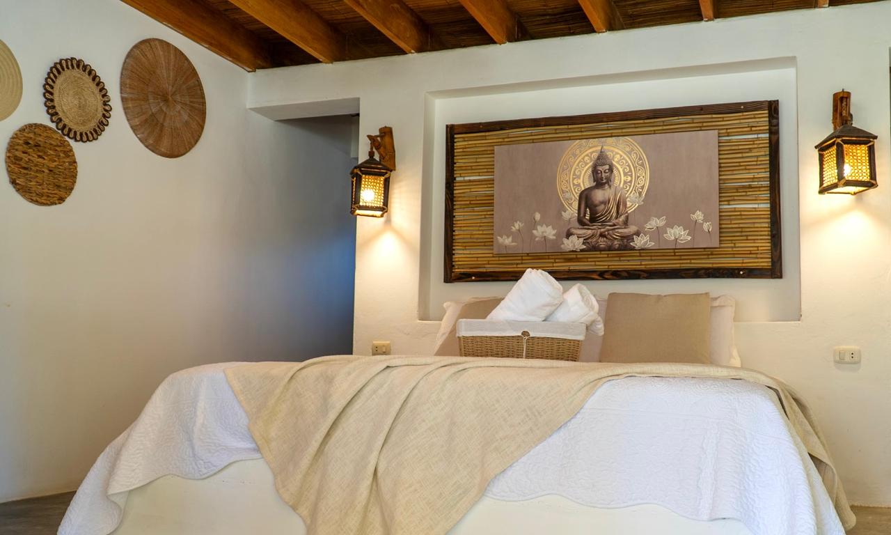 Mentawai Suite at Bali Lodge Hotel — double bed with golden halo Buddha artwork on bamboo backing, warm lanterns, woven wall decor, and quiet retreat ambiance