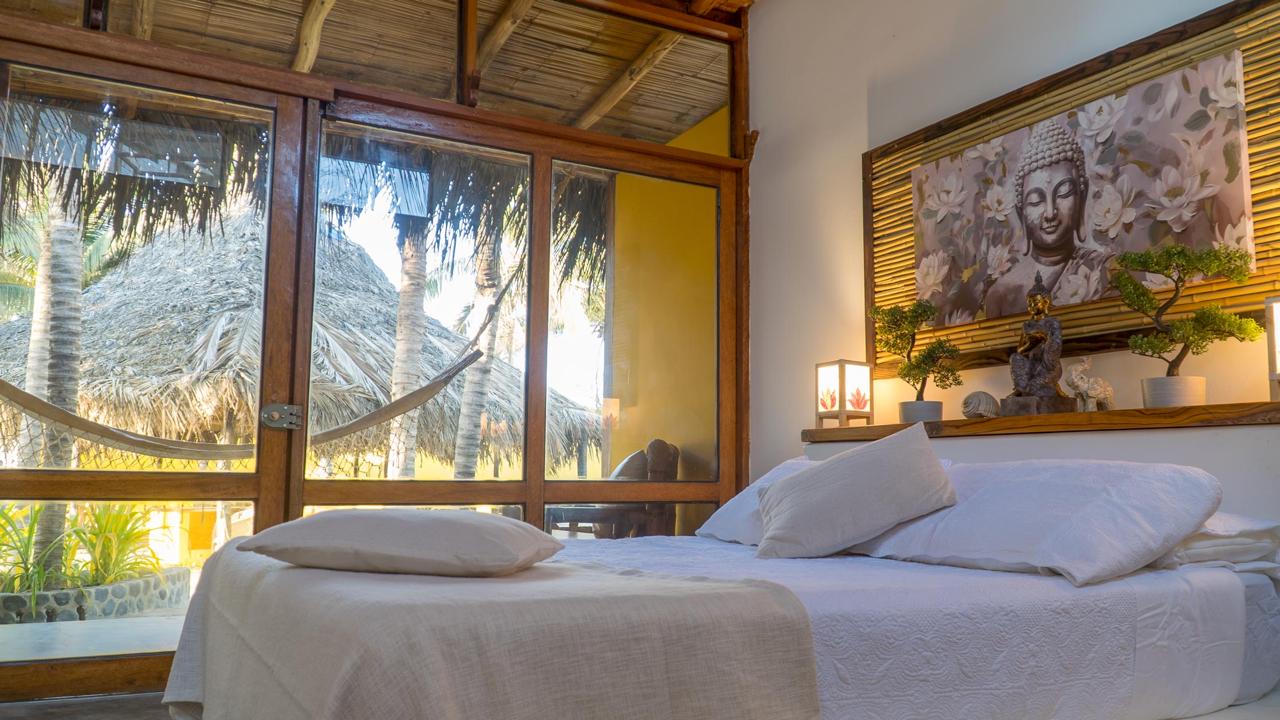 Bali Lodge room interior with bamboo ceiling, stone Buddha art, lantern light, and hammock patio outside
