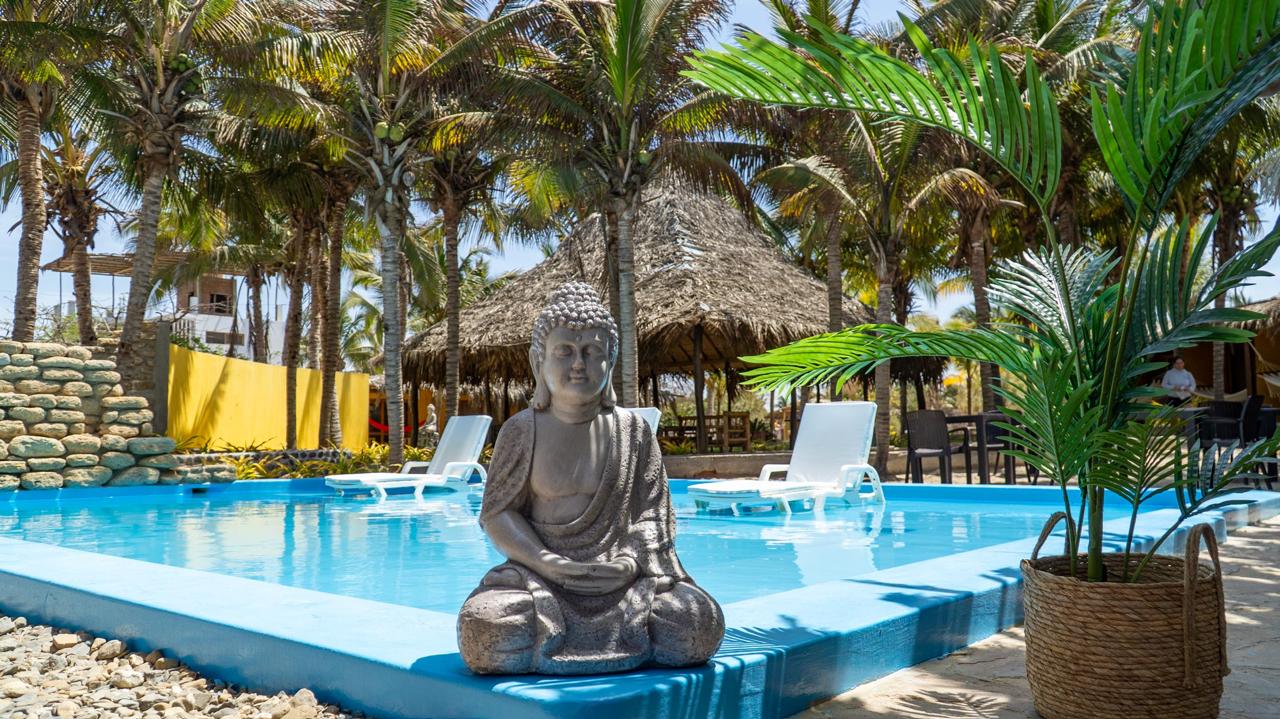 Bali Lodge swimming pool with meditating stone Buddha, coconut palms, palapa roof, and sun loungers in Máncora