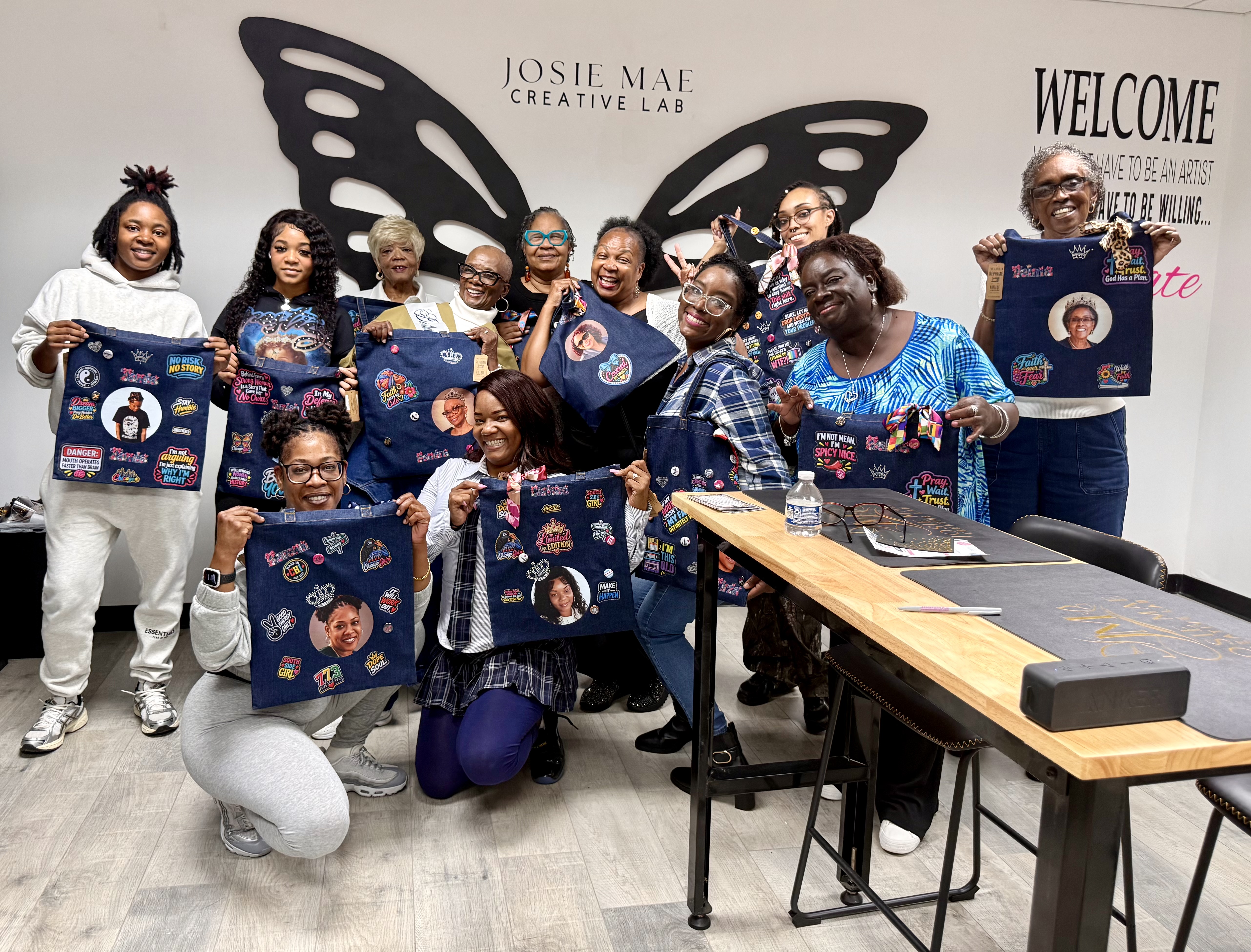 Guests proudly displaying their personalized junk tote bags in front of the butterfly wings at Josie Mae Creative Lab