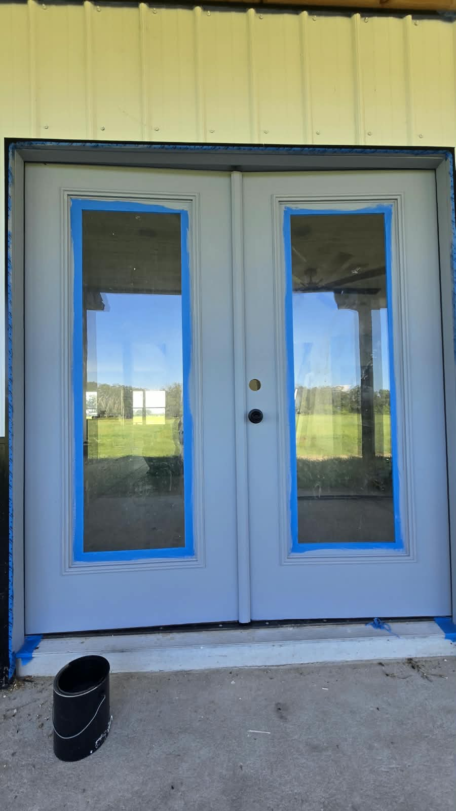 Double entry door glass perimeter masking with blue painter's tape before finish coat application
