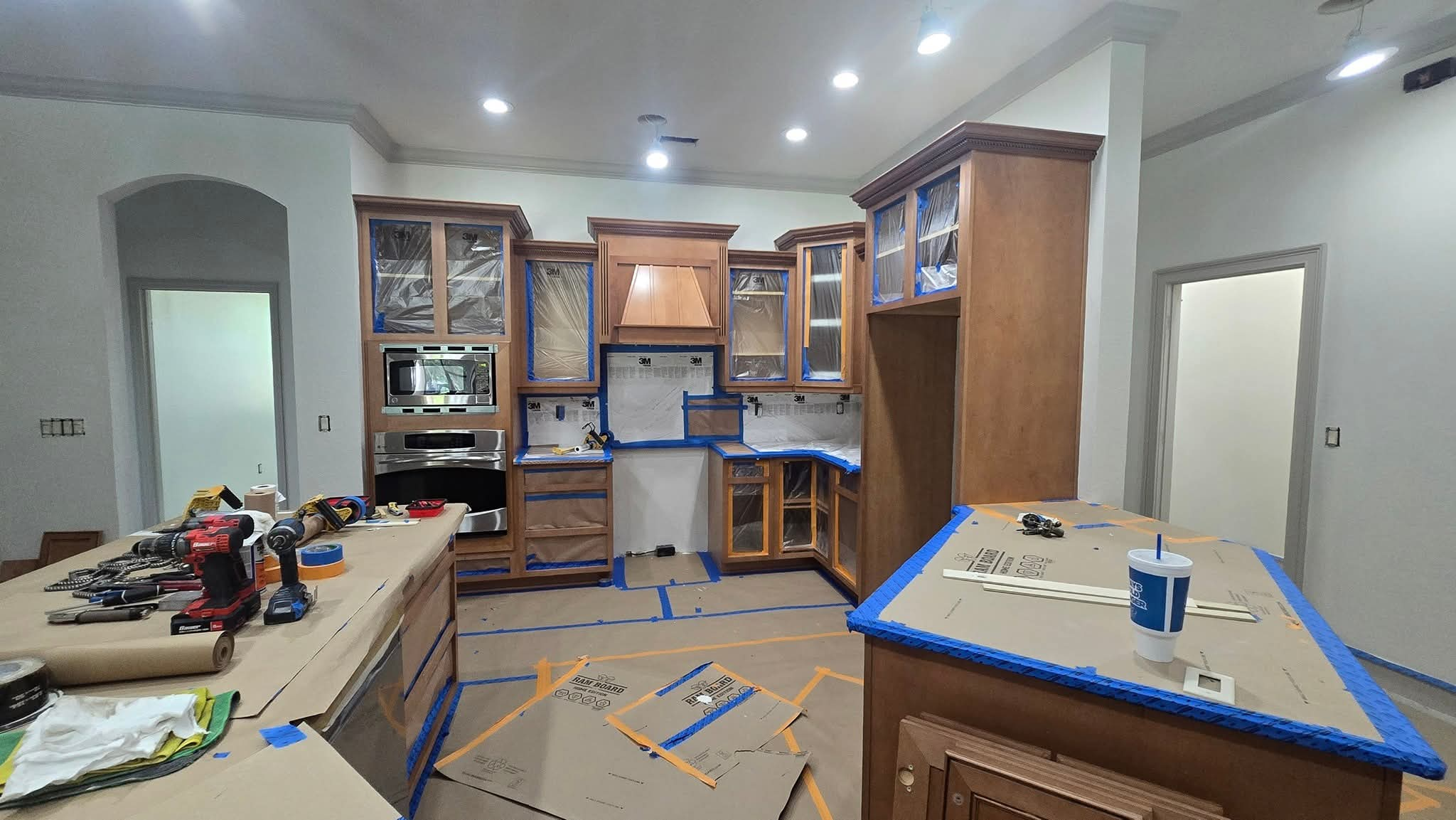 Original wood-tone kitchen cabinets during masking and spray preparation