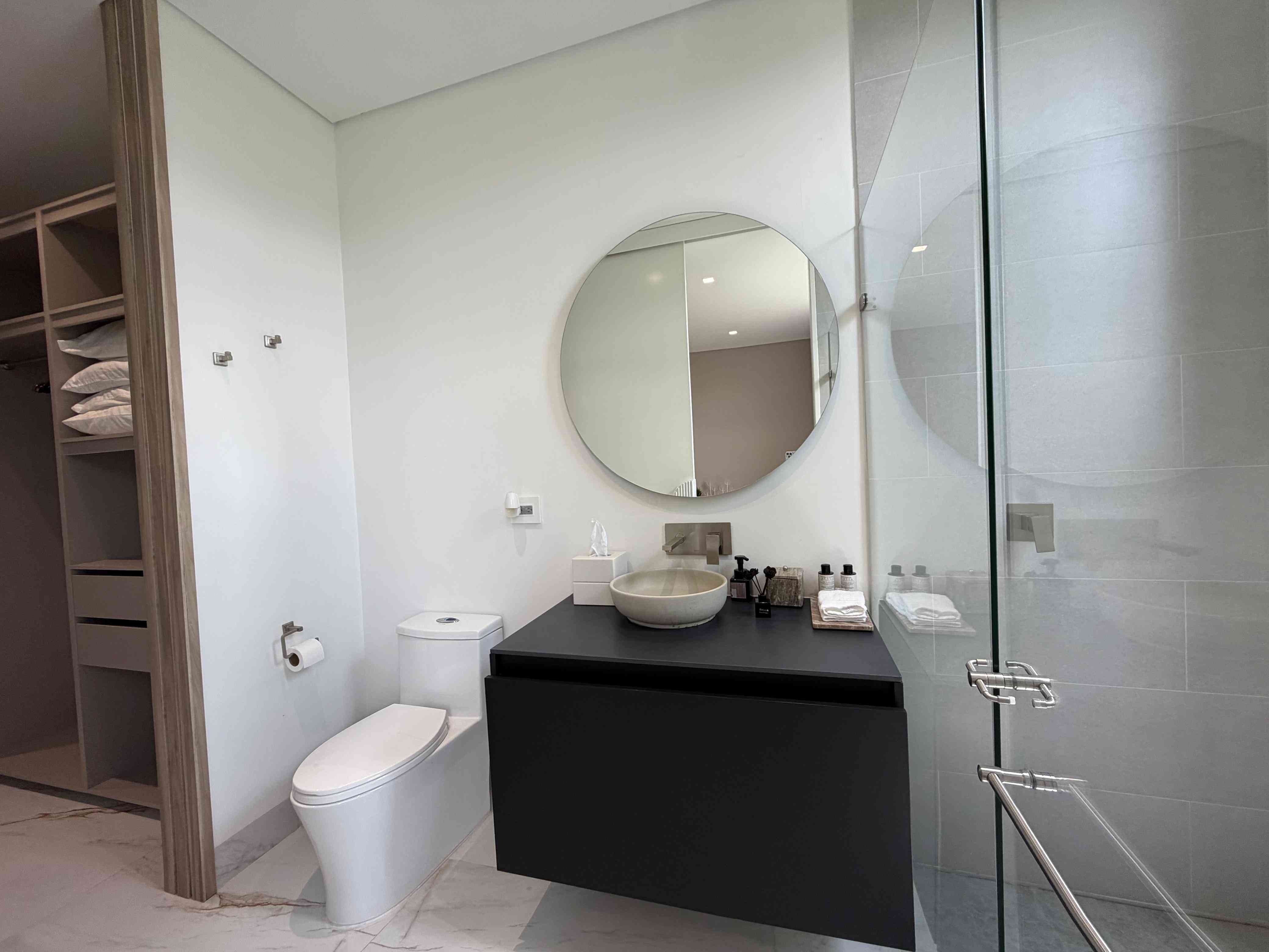 Baño en suite con mueble flotante negro, lavamanos en piedra y ducha de vidrio