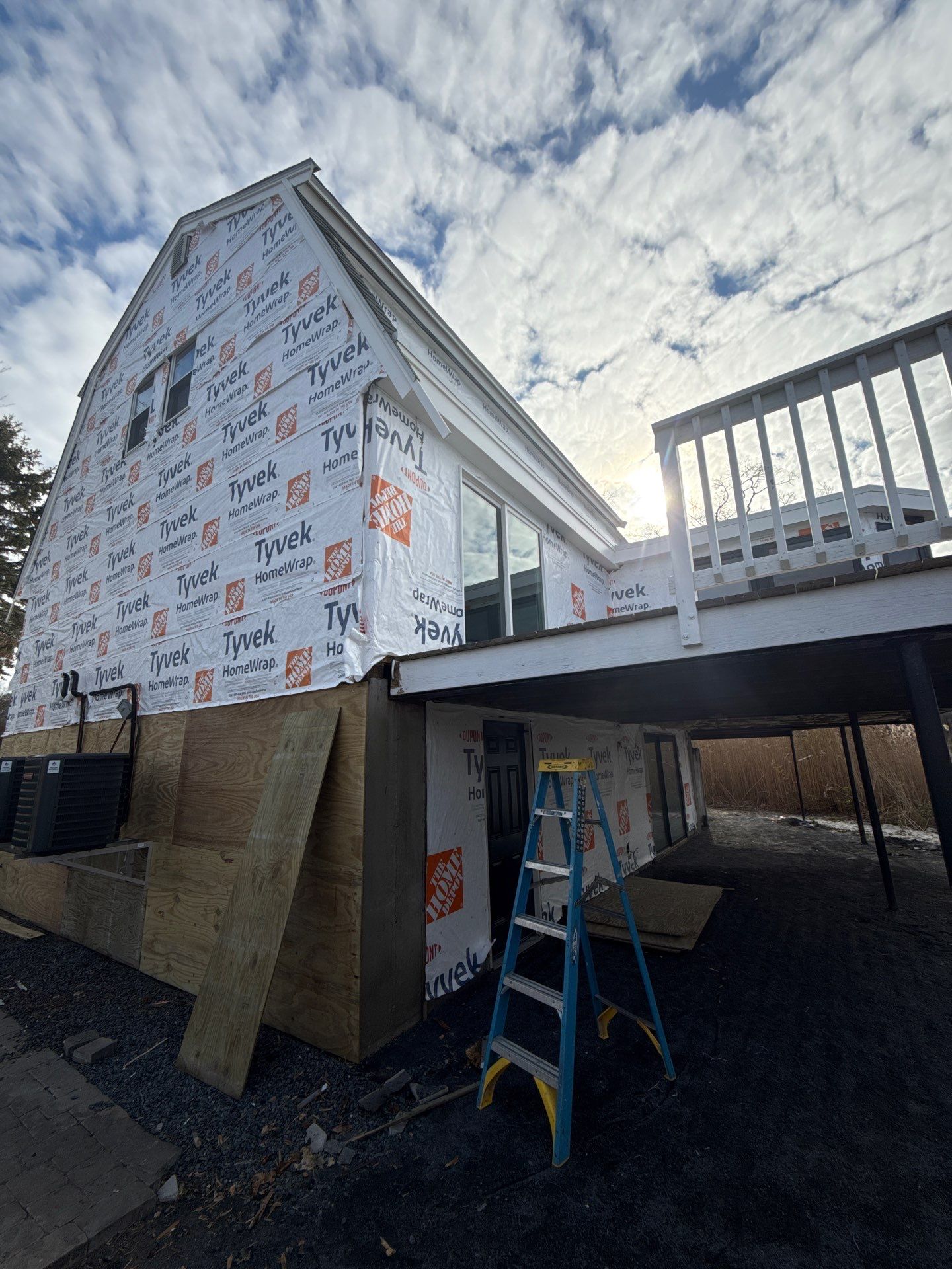 Before siding installation: multi-story home with exposed weather wrap moisture barrier and bare plywood sheathing ready for new siding