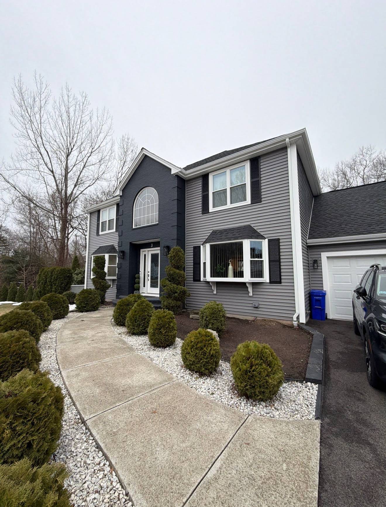 Completed exterior of a two-story Massachusetts colonial with charcoal grey siding, bold black entry arch facade, and white trim
