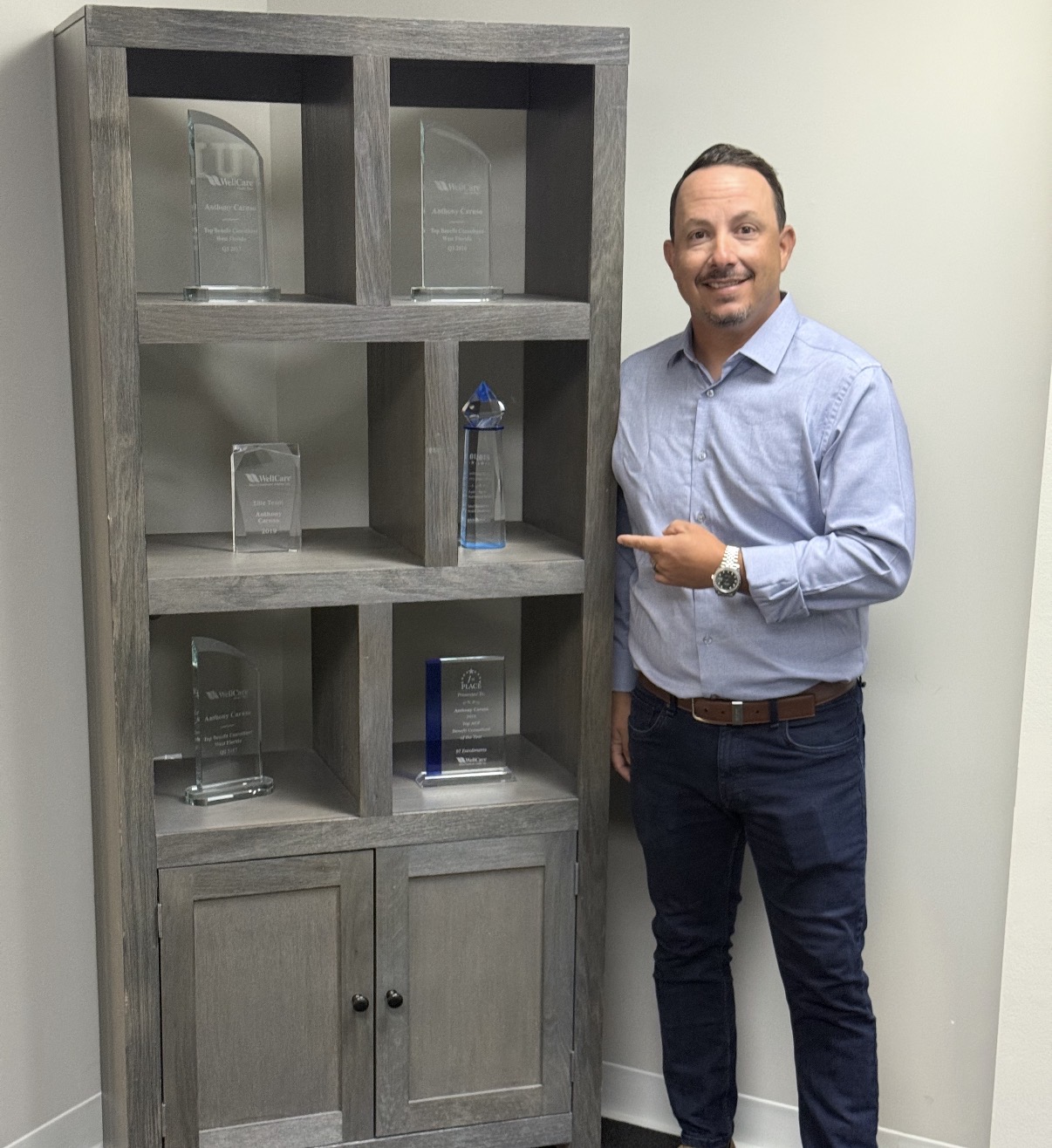 Anthony Caruso standing beside a cabinet displaying his insurance industry awards
