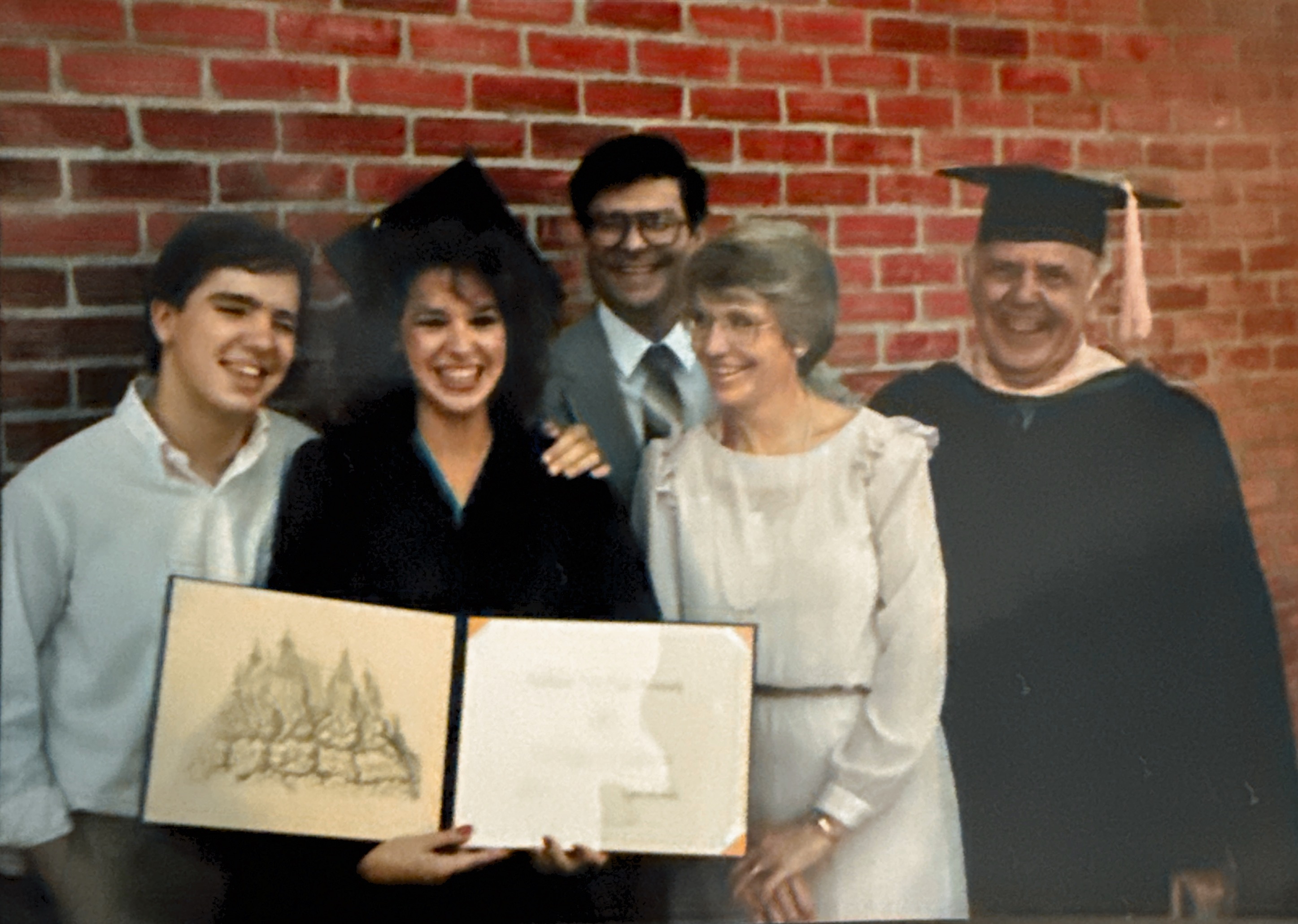 Laurie Winckel at her 1987 college graduation at Southwest Texas State University, holding her diploma alongside her voice teacher Harry Wayne (in black graduation attire)