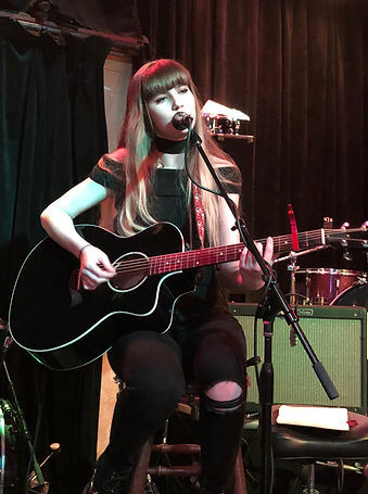 Kat Whitlock singing and playing acoustic guitar live on stage
