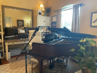 Inside the Vocal Edge Studio voice lesson room with grand piano, microphone, comfortable seating, and warm lighting