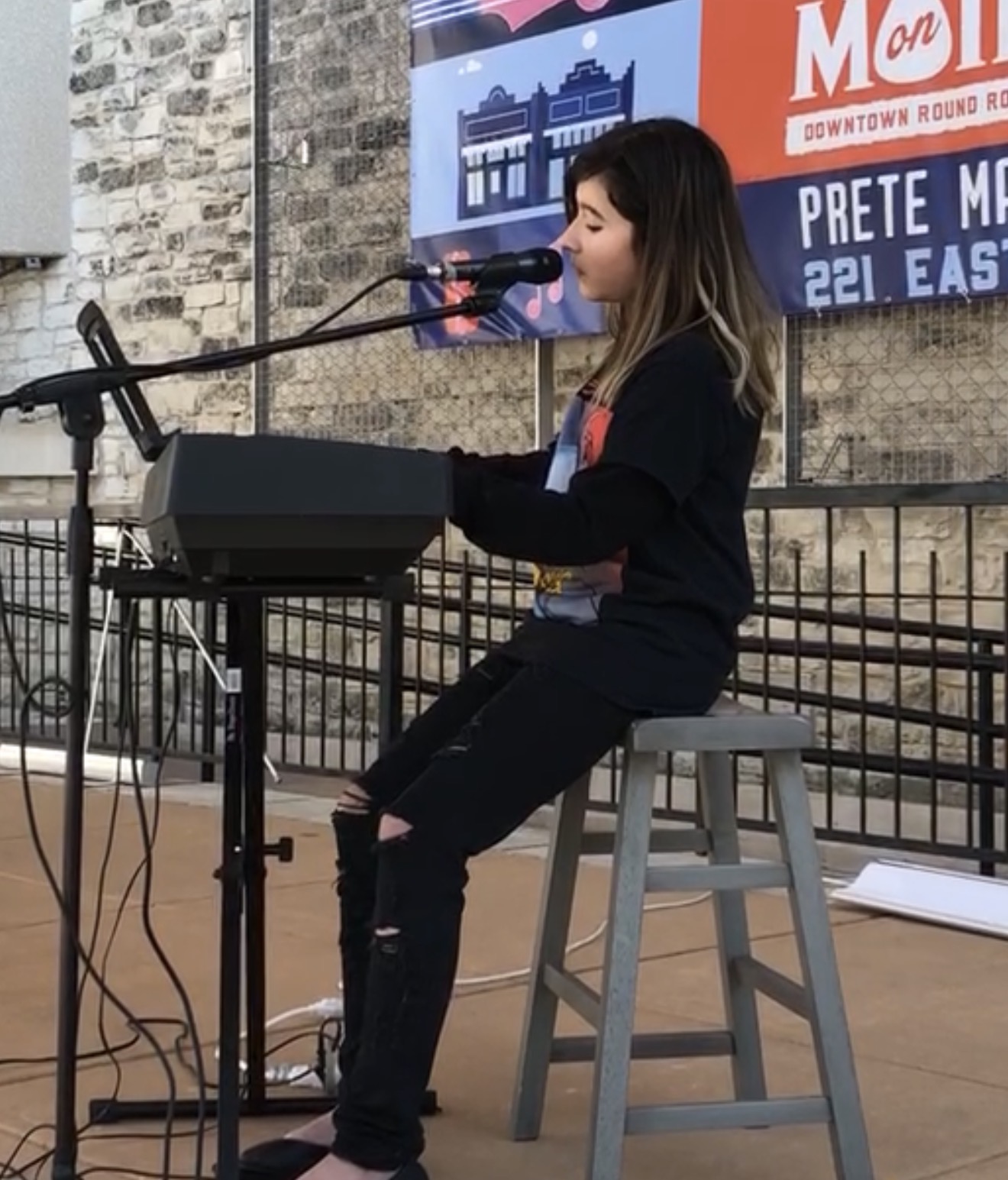 Student singing and playing keyboard at an outdoor live performance stage