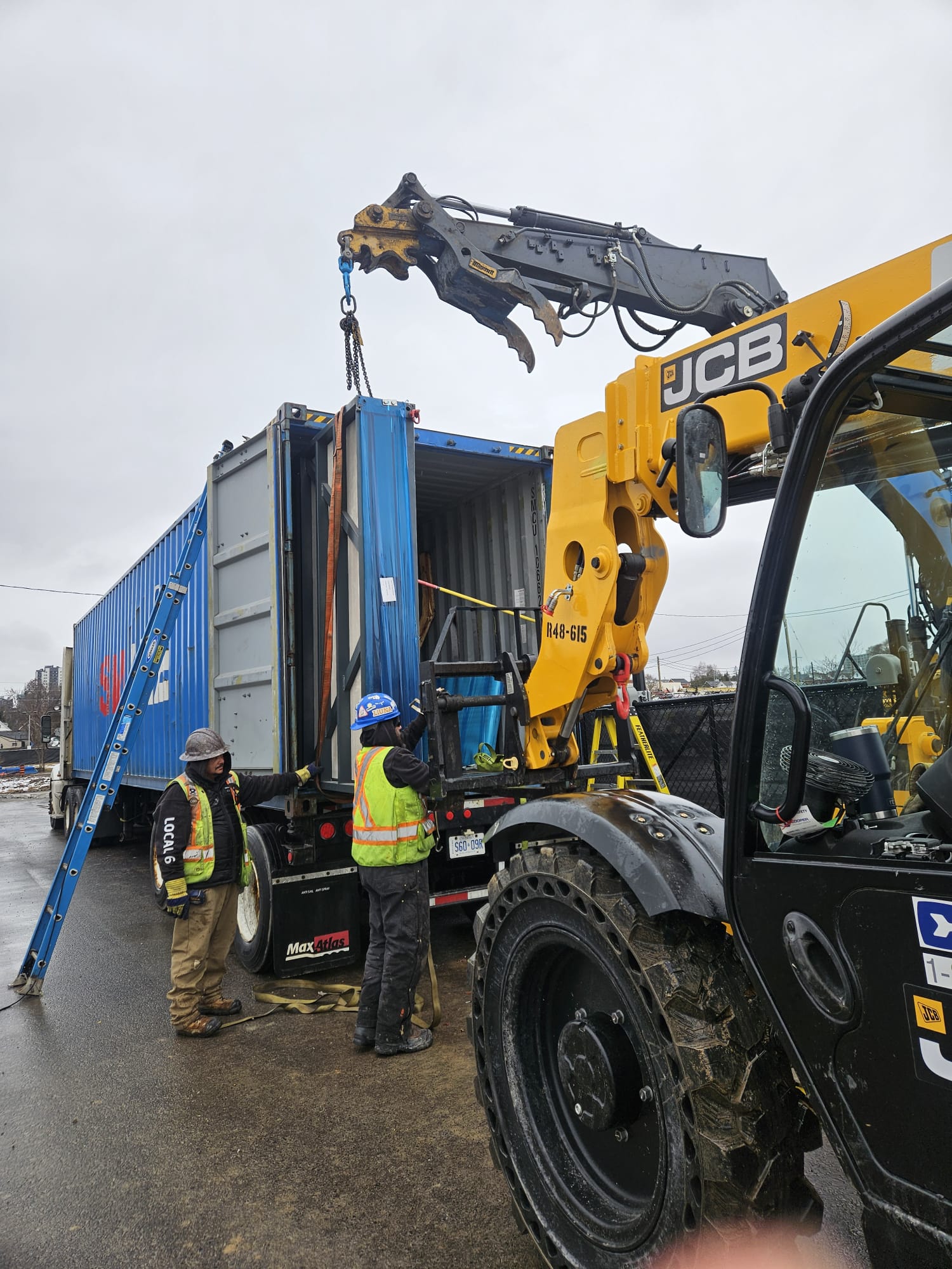 Forklift and crew offloading folded modular microshelter units directly from shipping container