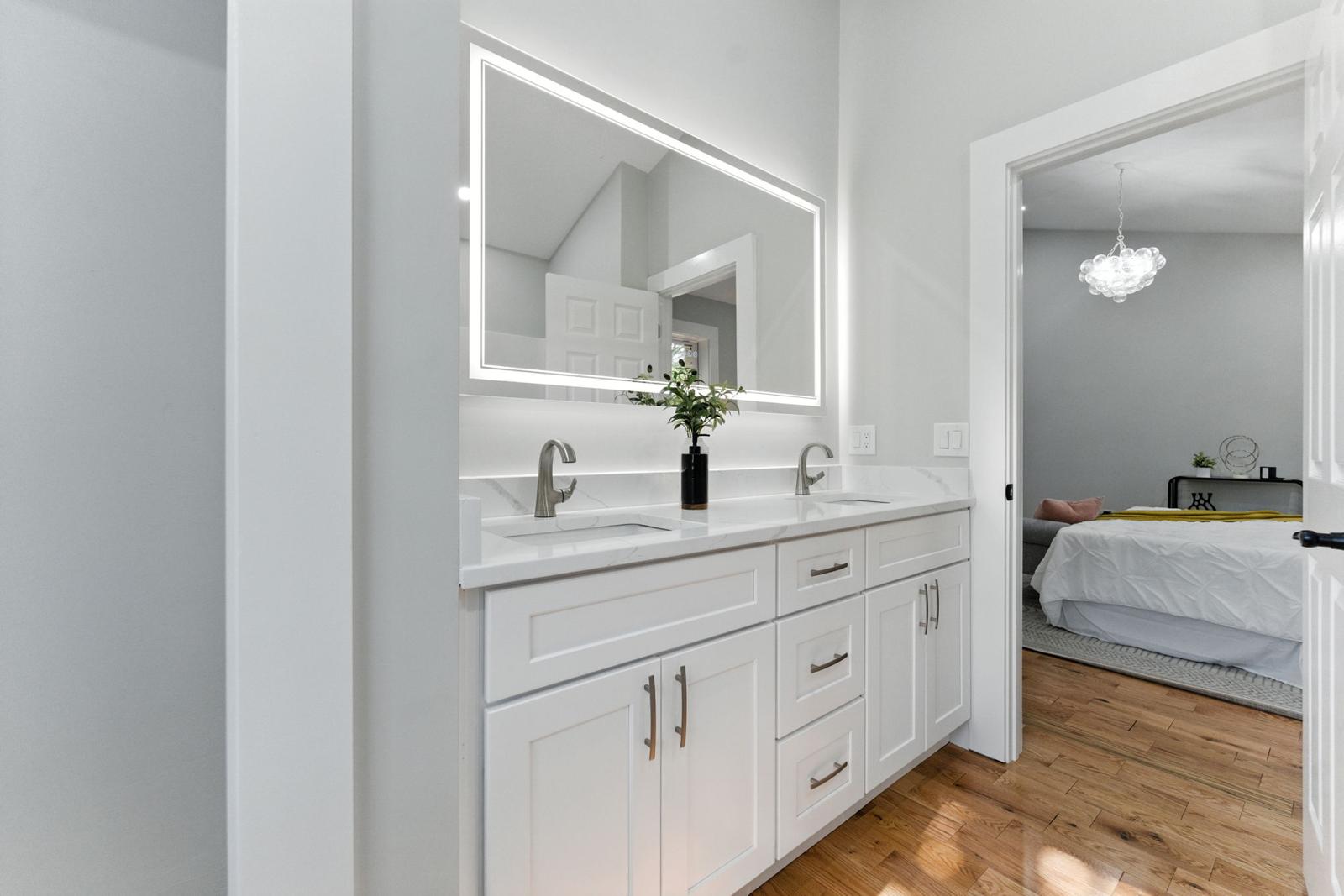 Modern luxury bathroom with perimeter illuminated LED vanity mirror and view to bedroom chandelier by Prime Light Electric LLC in Westborough MA