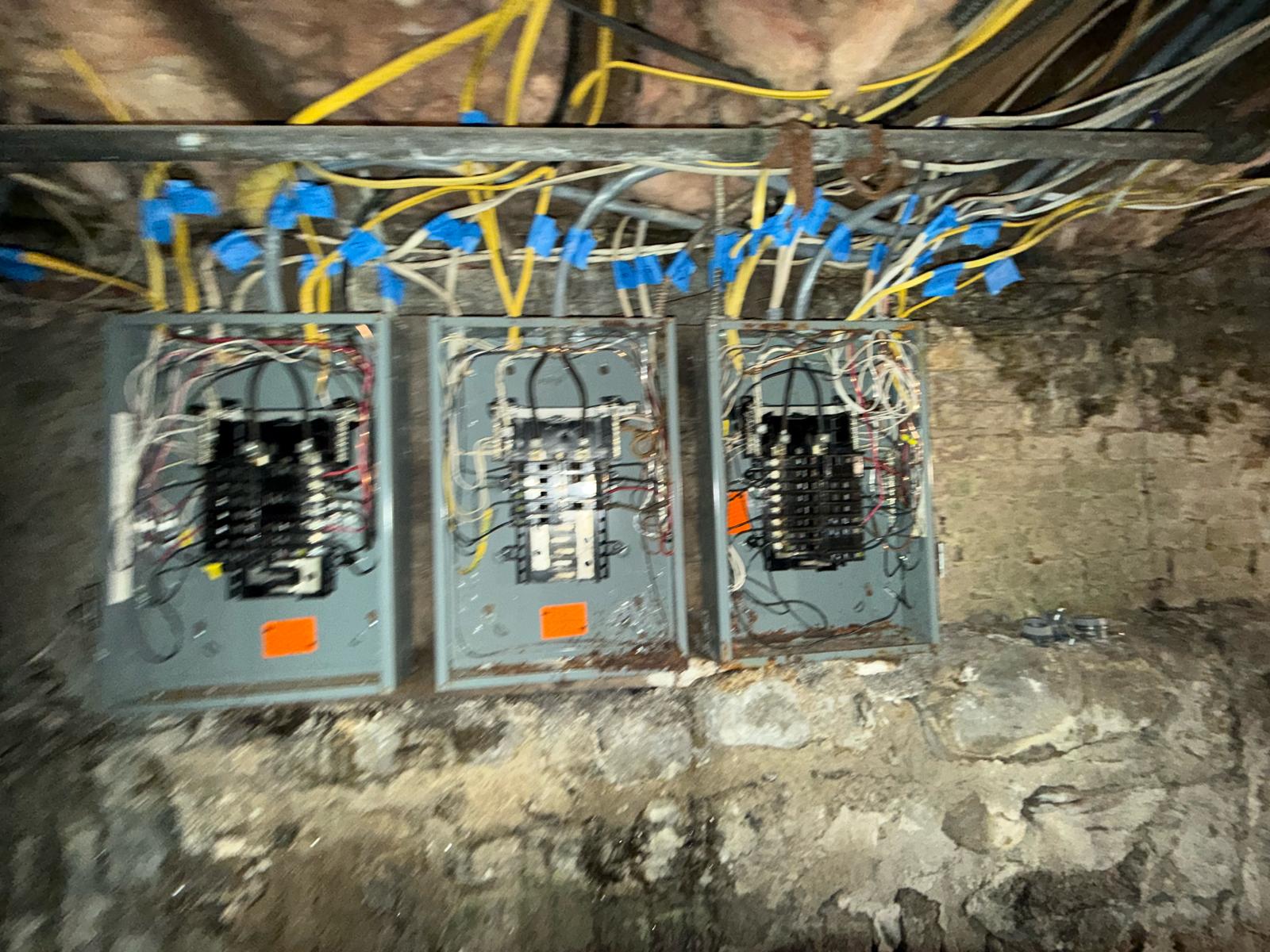 Three multi-family electrical service panels tagged for branch rewiring along stone basement wall by Prime Light Electric LLC in Worcester MA