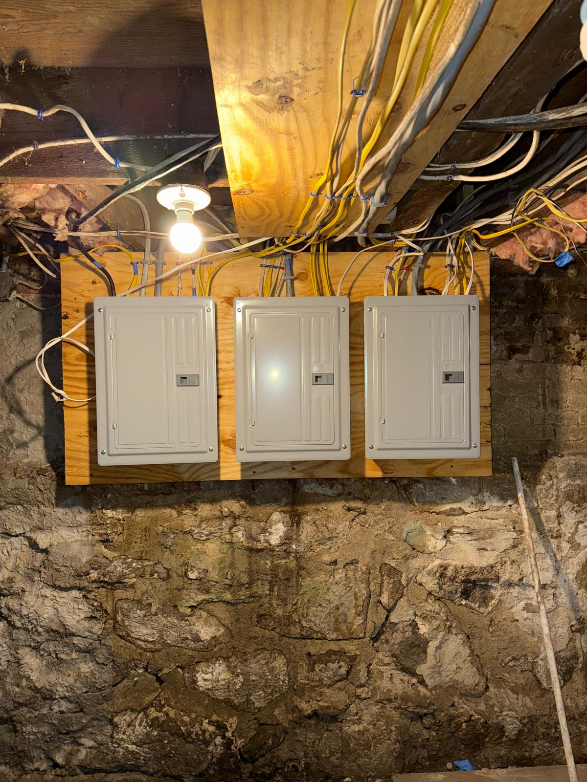 Three finished breaker panels mounted on wood backer board on stone foundation wall by Prime Light Electric LLC in Worcester MA