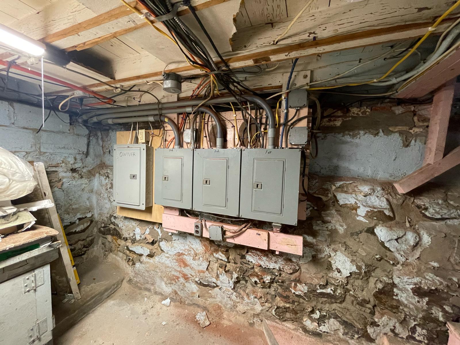 Multi-meter apartment breaker panels mounted on wood frame in stone basement by Prime Light Electric LLC in Millbury MA