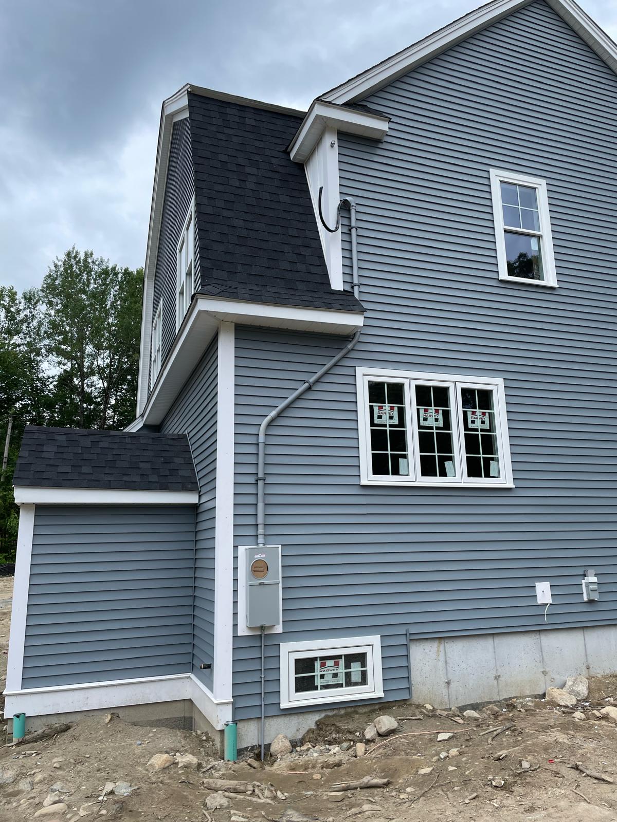 New home exterior meter combo panel with contoured overhead conduit riser on slate blue siding by Prime Light Electric LLC in Shrewsbury MA