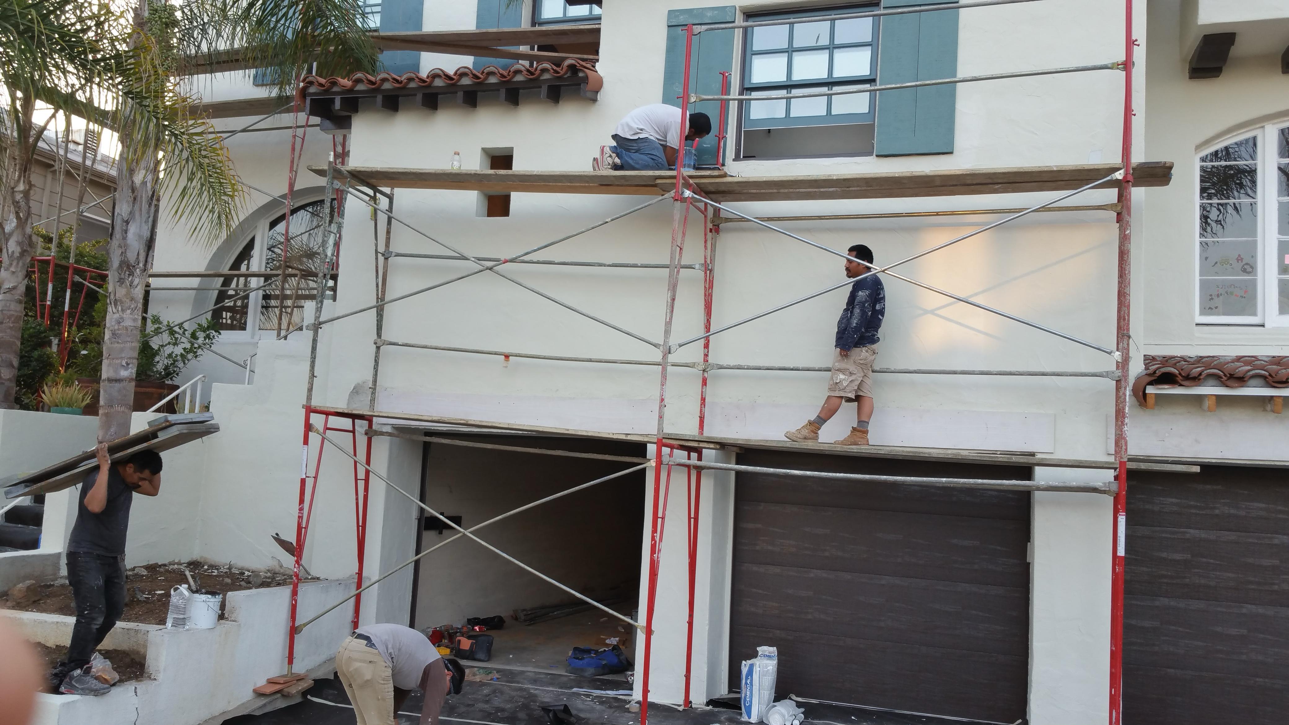 LA Builder team on multi-level exterior scaffolding completing window trim and stucco finishing on custom two-story Spanish style home