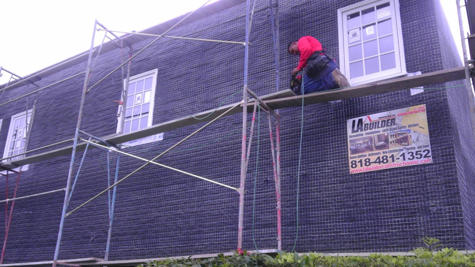 LA Builder Construction contractor working on scaffolding installing exterior wire lath and moisture barrier on residential two-story home in Los Angeles