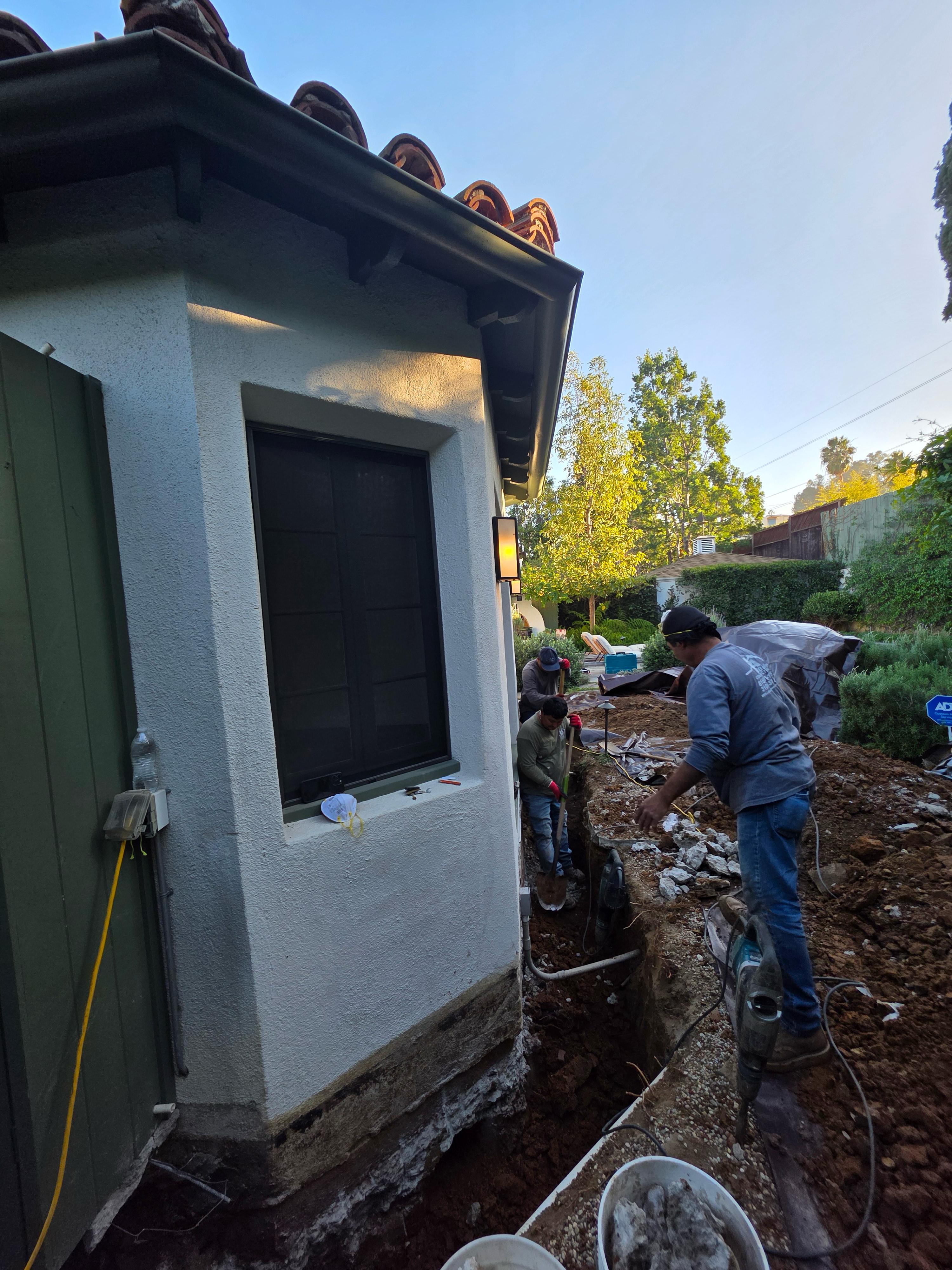 Deep perimeter excavation and concrete foundation underpinning trench with jackhammers alongside residential home by LA Builder crew