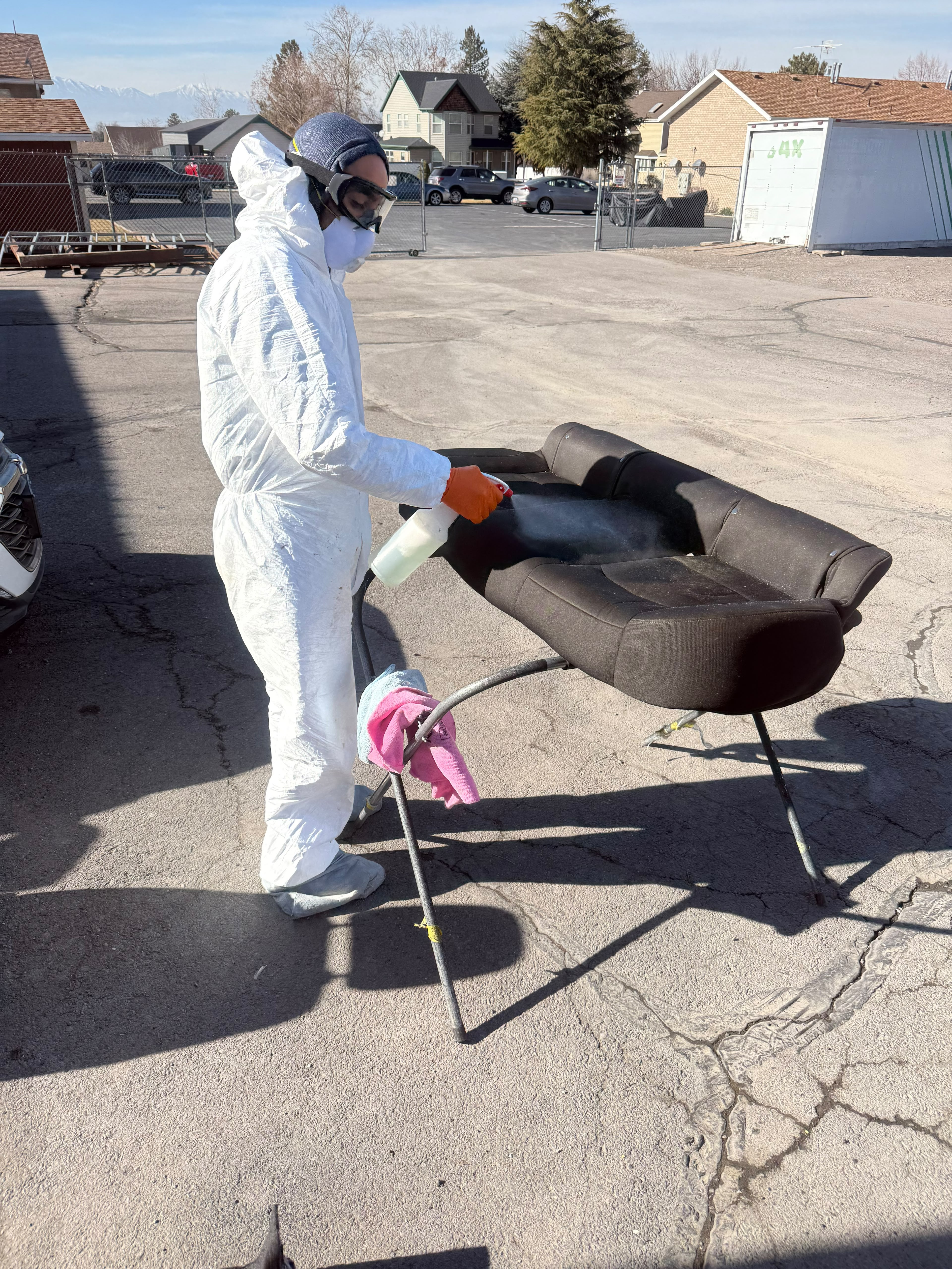 Detailer in full protective Tyvek suit applying professional chemical extraction solution onto removed rear seat by Miracle Detailing Lindon UT