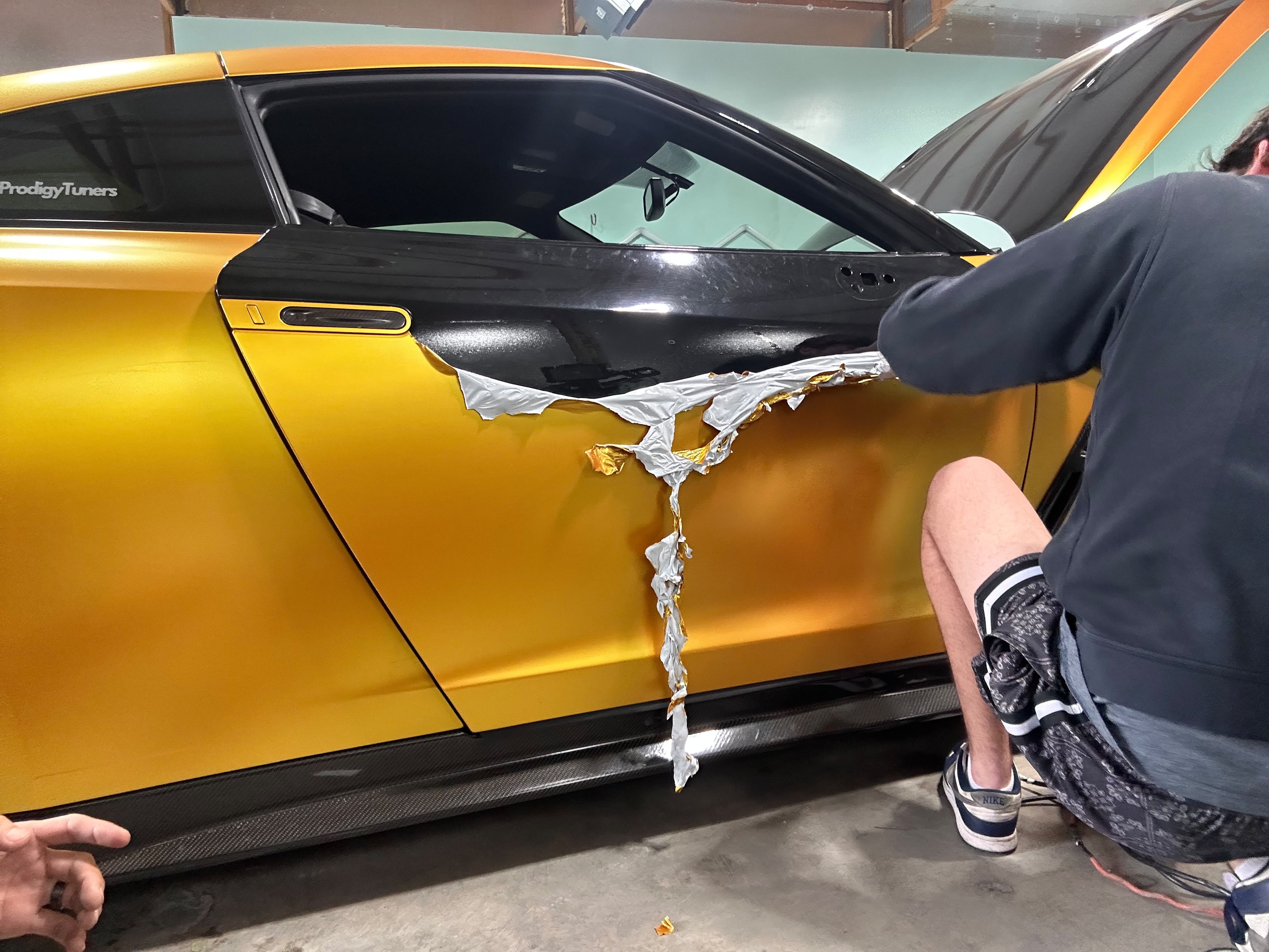 Nissan GT-R sports car metallic gold vinyl wrap removal and door paint restoration in shop bay by Miracle Detailing