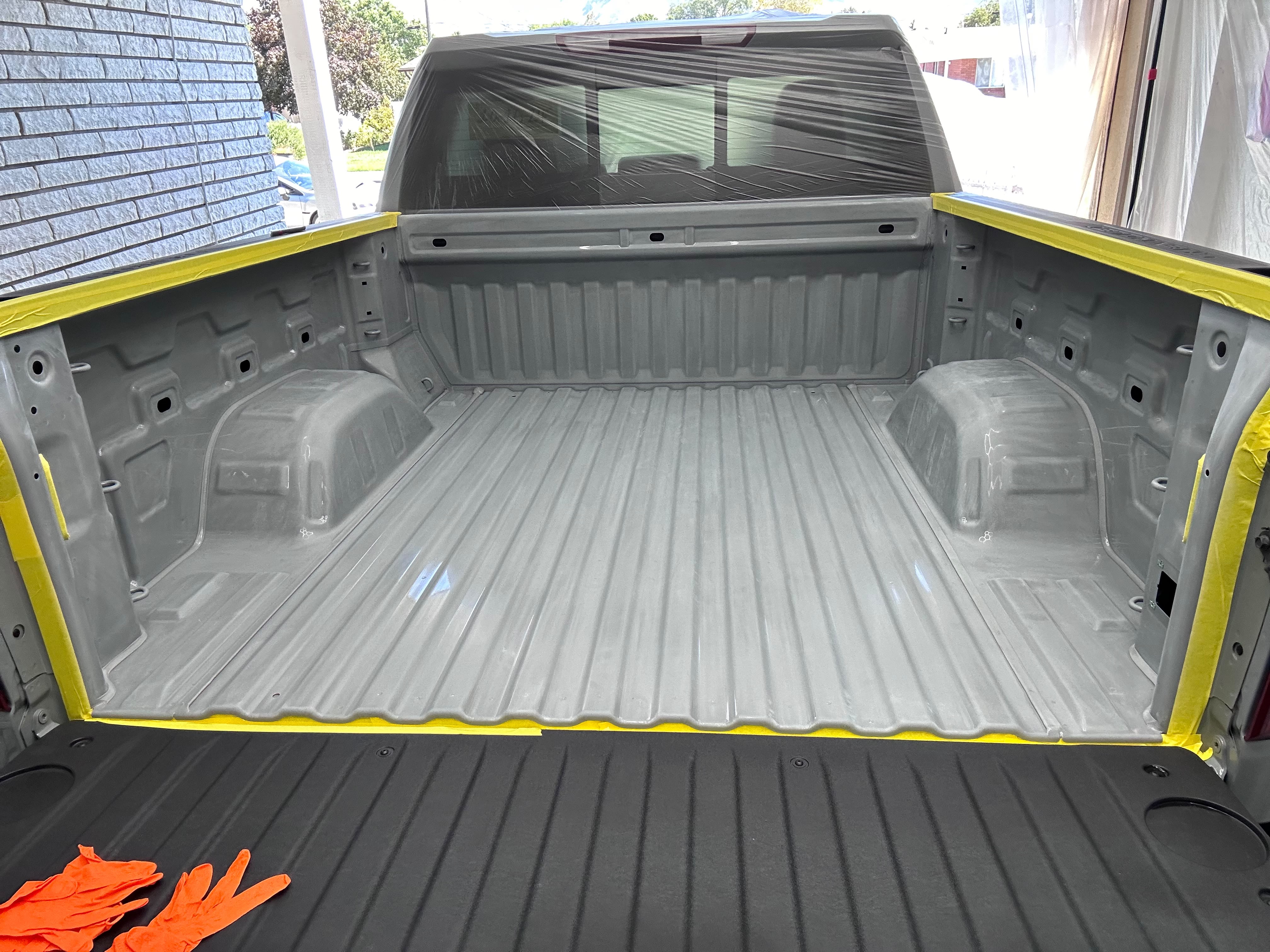 Truck bed and cab wrapped with protective film and yellow edge tape before Rhino Lining spray application by Miracle Detailing