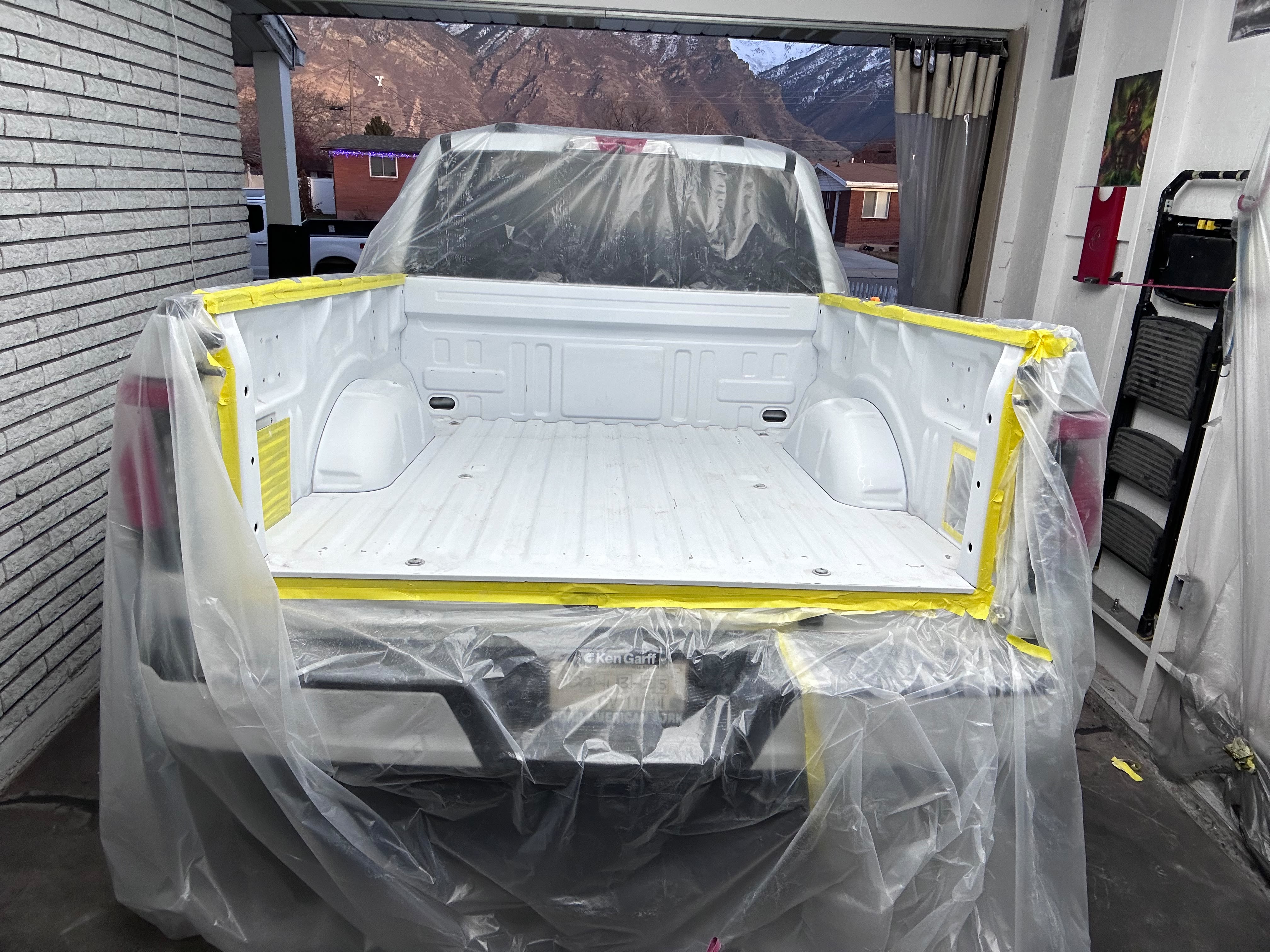 White Ford pickup truck bed and cab exterior fully plastic-sheeted and edge-taped for spray-in bed liner in Lindon UT shop bay by Miracle Detailing