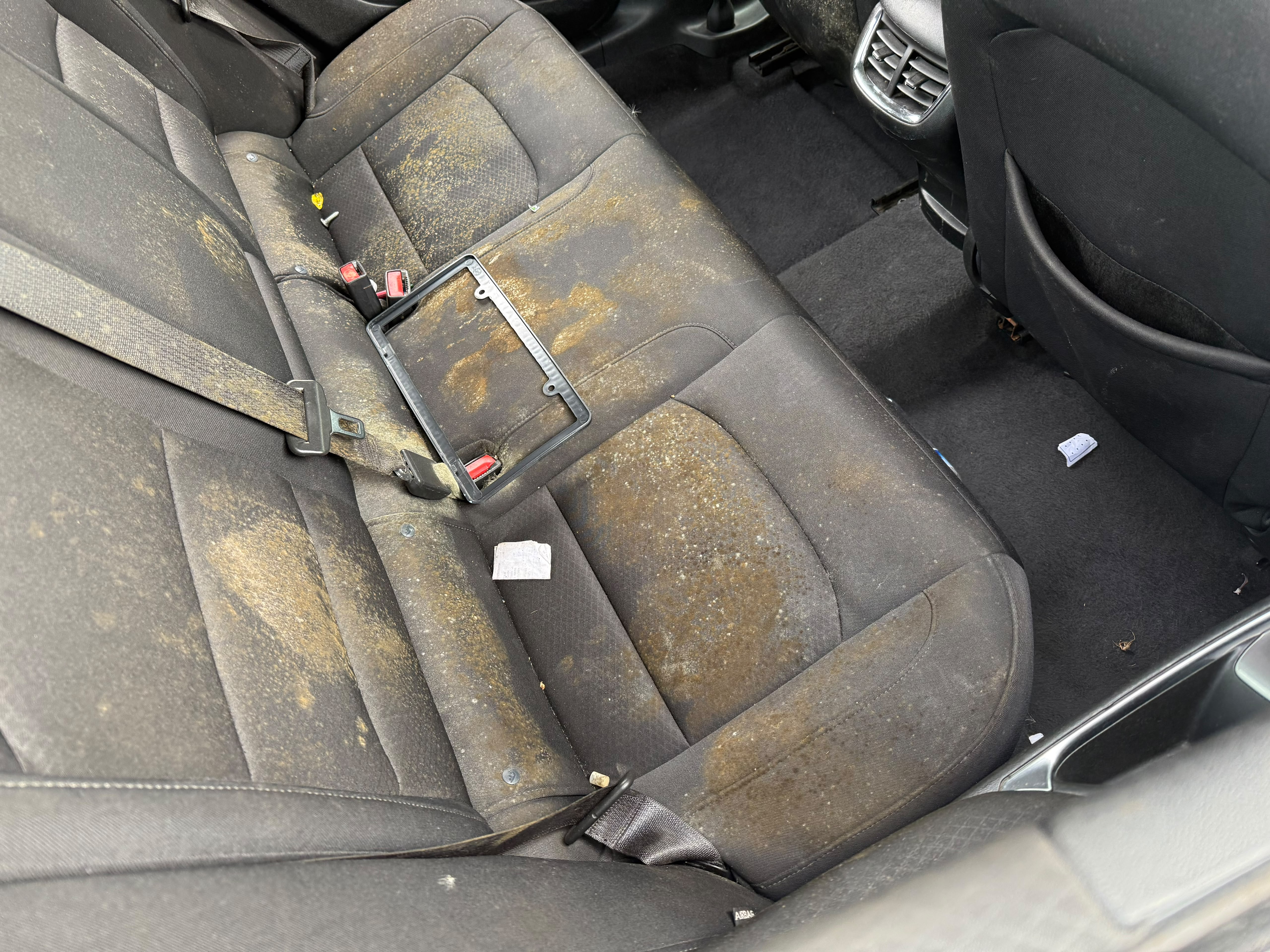 Vehicle rear passenger cloth seats covered in heavy dirt, spilled residue, and mildew before deep steam extraction by Miracle Detailing