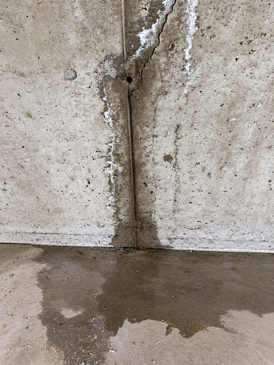 Concrete wall crack with visible water staining and moisture at the floor before repair