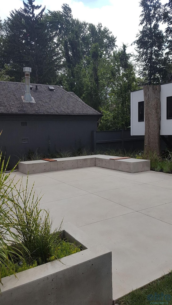 Modern residential concrete patio with low concrete seating walls and landscaped garden.