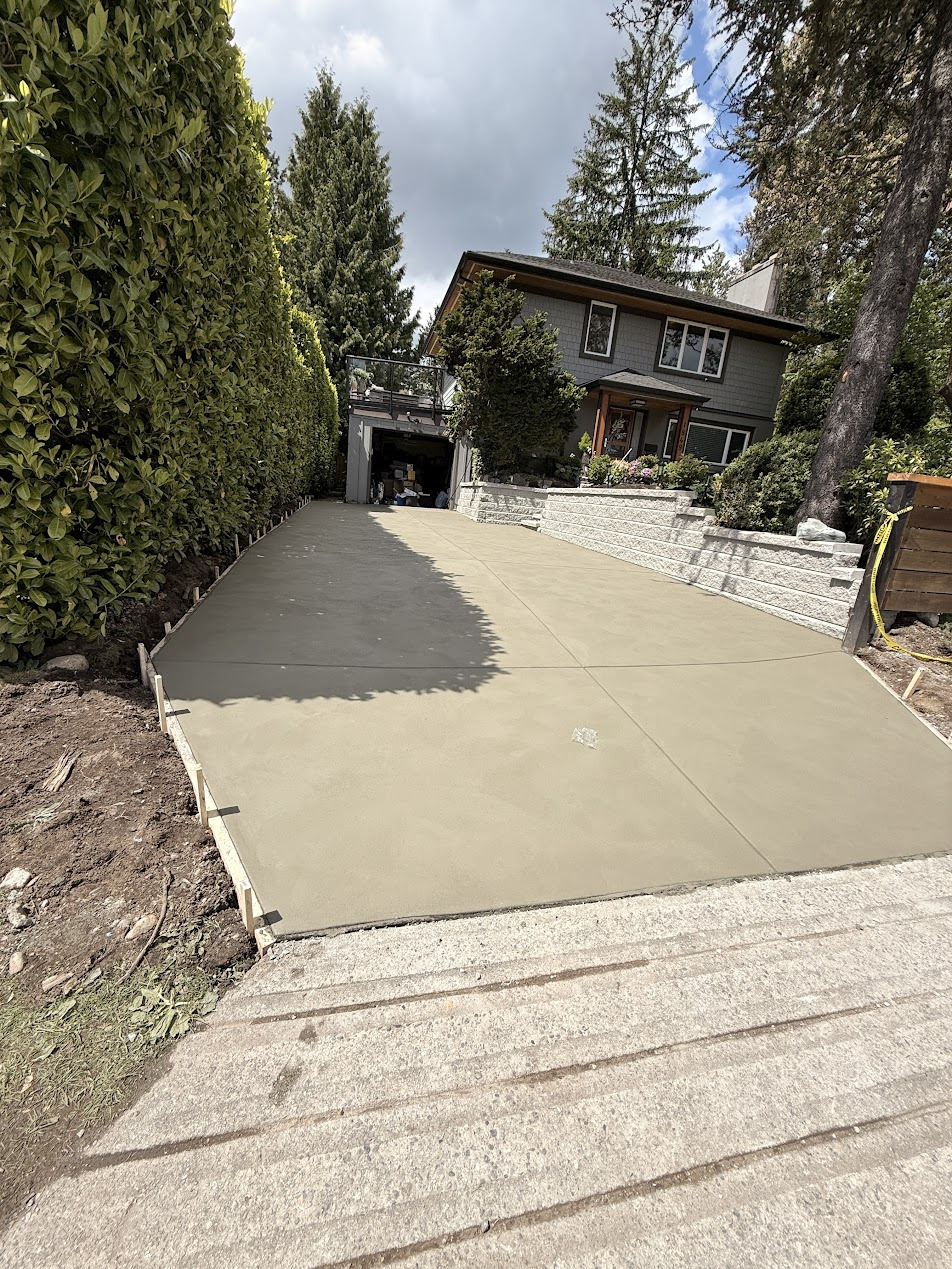 Concrete driveway between a tall hedge and stepped retaining walls, with edge formwork still in place.