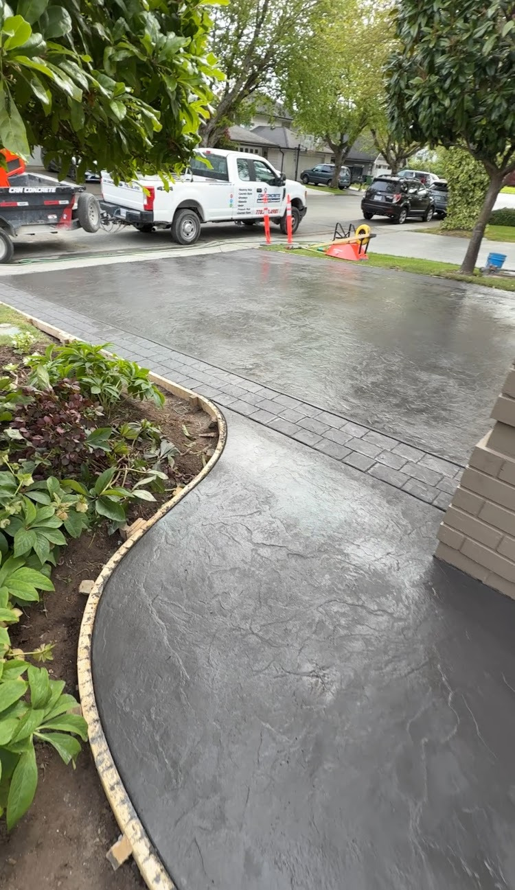Textured concrete walkway curving around a planting bed and connecting to a driveway with a patterned border.