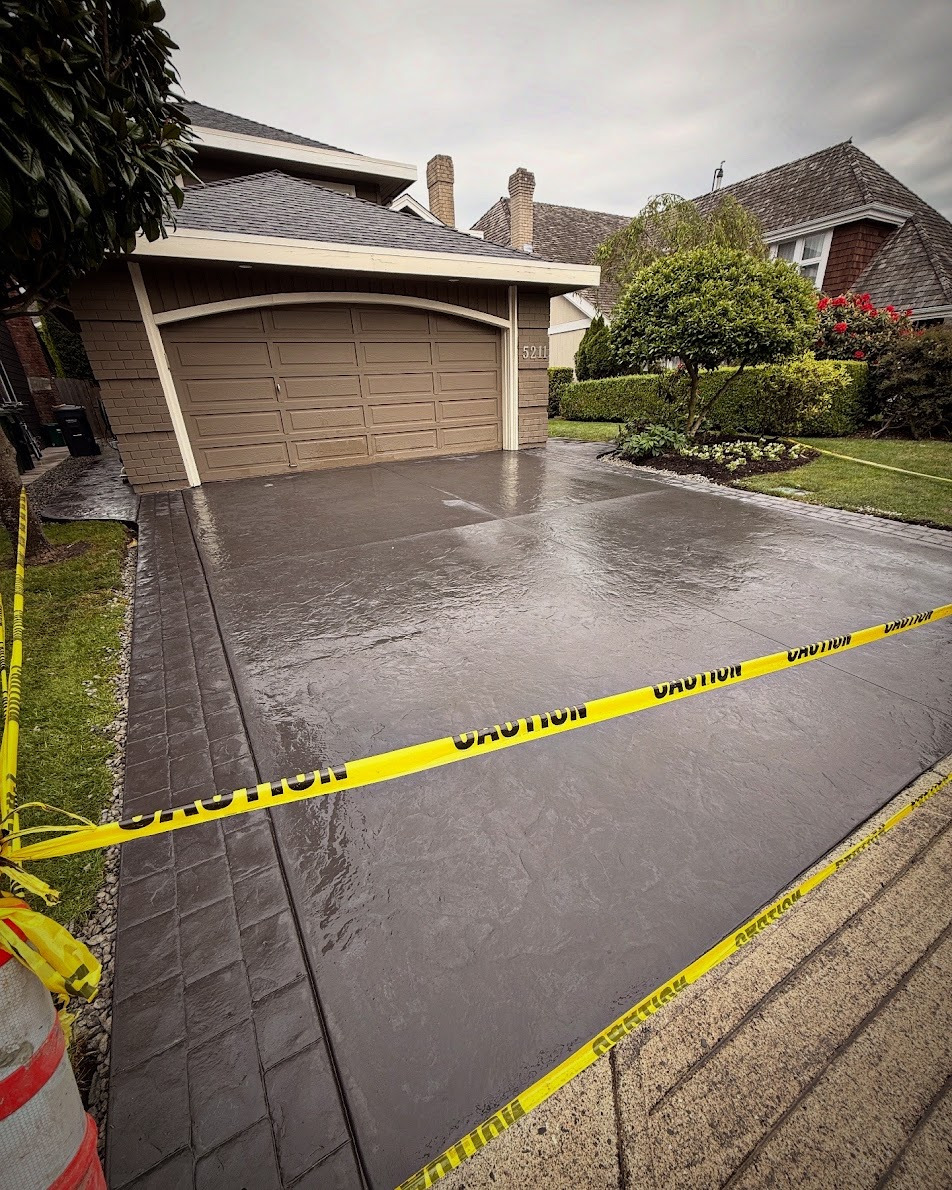 Grey textured concrete driveway with a patterned border in front of a garage, protected by caution tape.