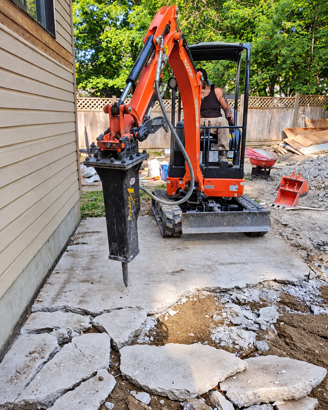 Mini excavator breaking and removing existing concrete during site preparation.