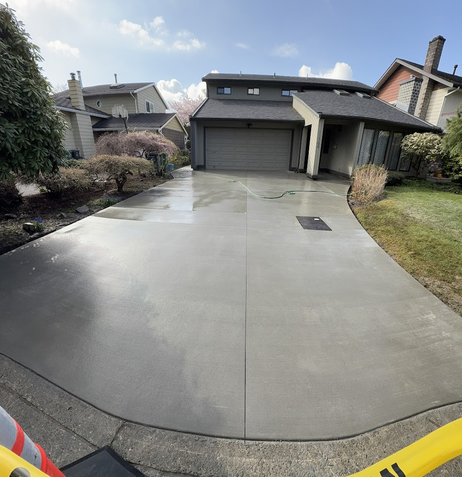 Concrete driveway leading to a residential garage, with a hose and caution tape visible.