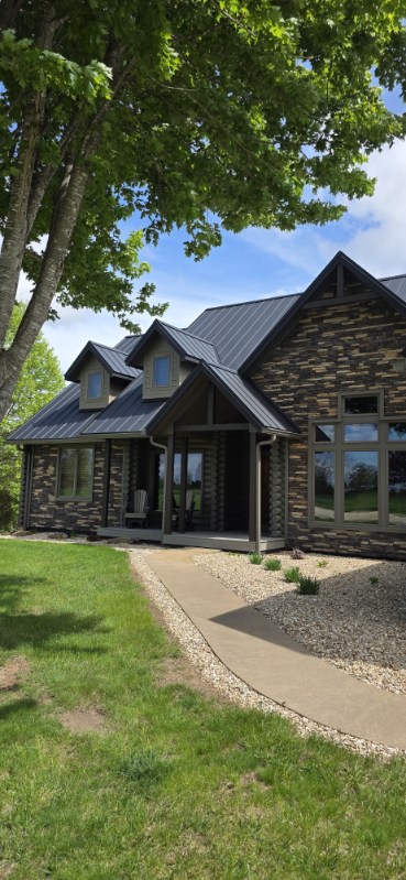 Stone and timber entry of a home with a dark standing seam metal roof and dormers, roofed by Snaplock Roofing LLC