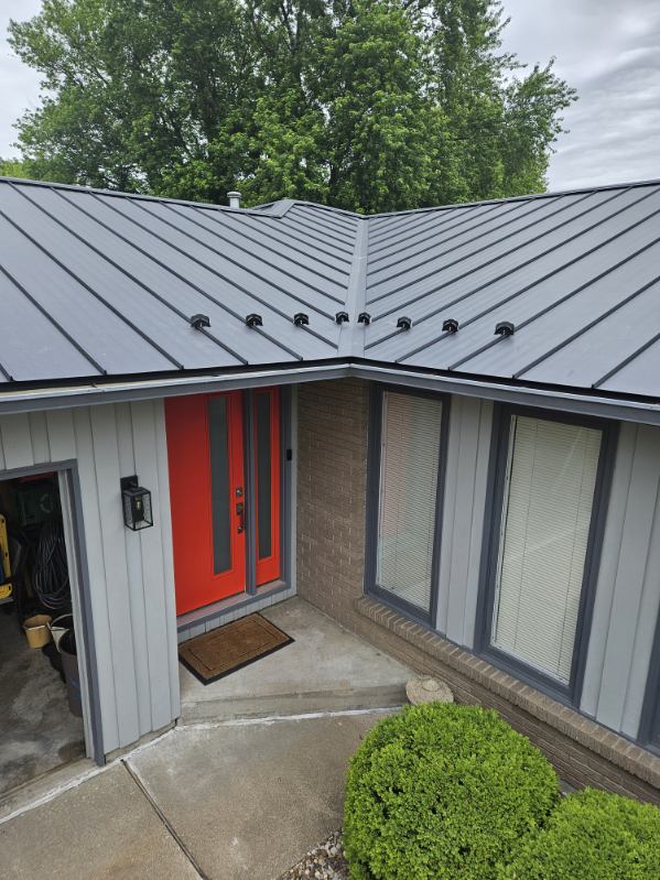 Close view of a dark standing seam metal roof with snow guards above an entryway, installed by Snaplock Roofing LLC