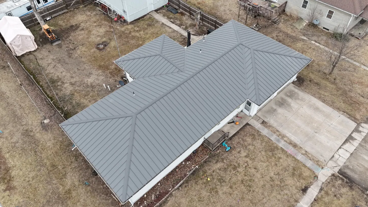 Overhead view of a grey standing seam metal hip roof showing four roof planes, a valley and mitred hip cuts, installed by Snaplock Roofing LLC