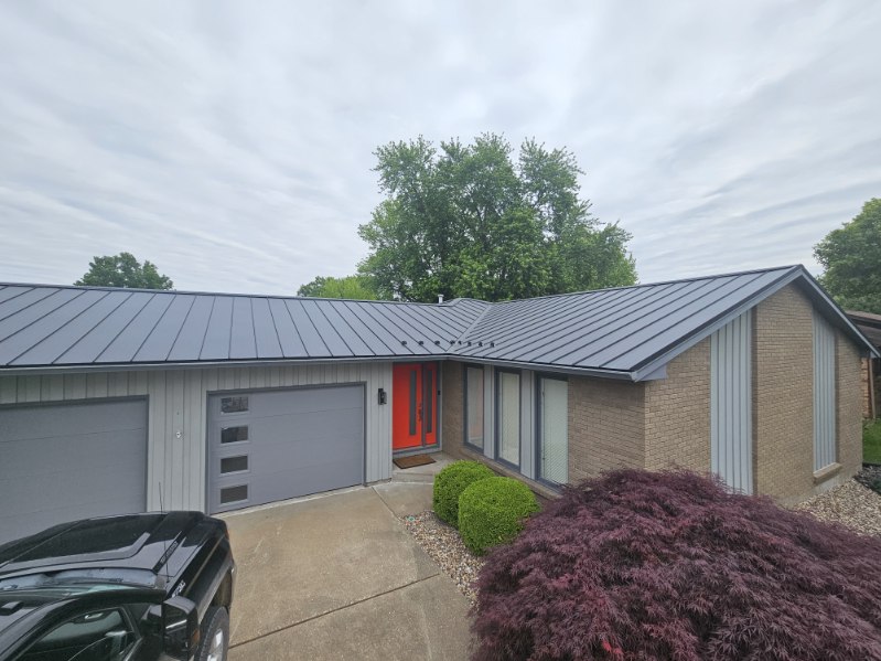 Close view of a dark standing seam metal roof on a brick ranch home, showing the seams and ridge, installed by Snaplock Roofing LLC