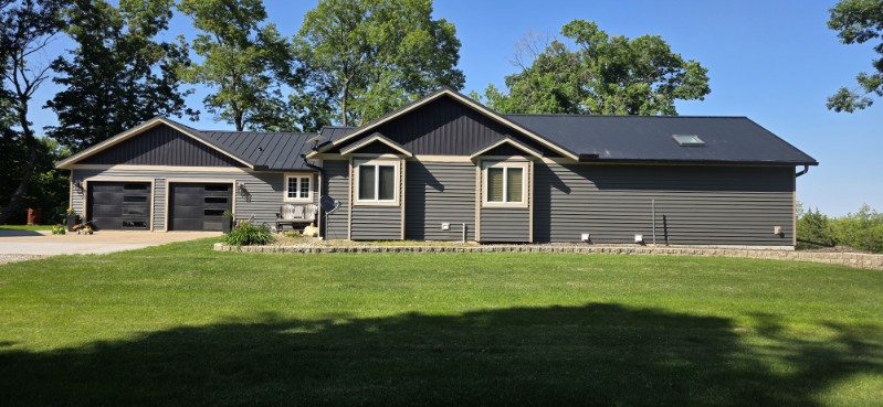 Board and batten steel siding on the gable ends of a ranch home with a dark standing seam metal roof, installed by Snaplock Roofing LLC