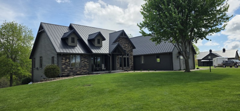 Home and detached outbuilding with matching dark standing seam metal roofs, installed by Snaplock Roofing LLC