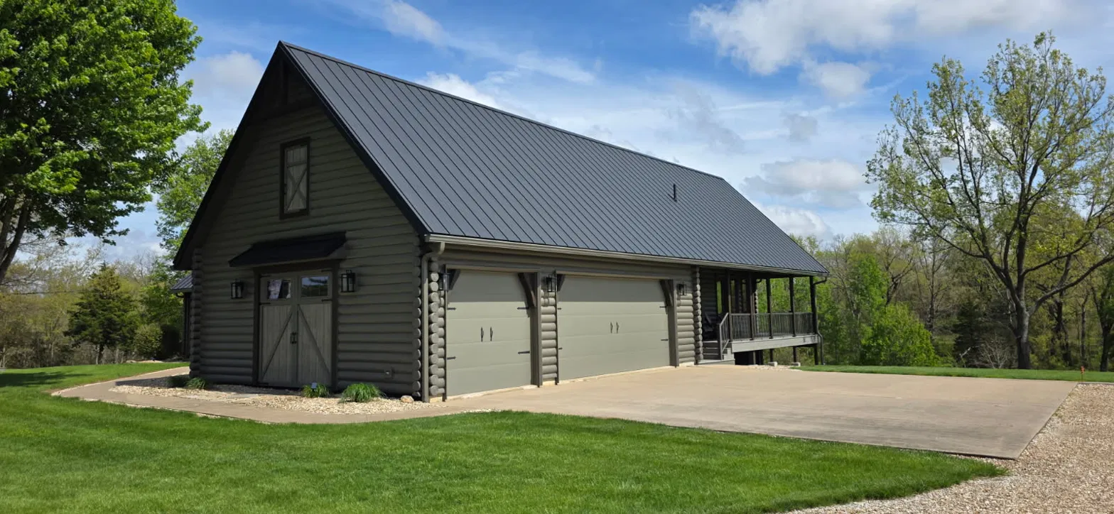 Log garage with living space under a black standing seam metal roof and a covered porch, roofed by Snaplock Roofing LLC