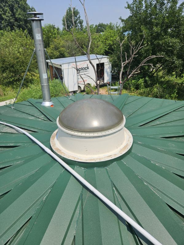 Tapered green metal roof panels radiating from a center dome on a round building, roll-formed on site by Snaplock Roofing LLC