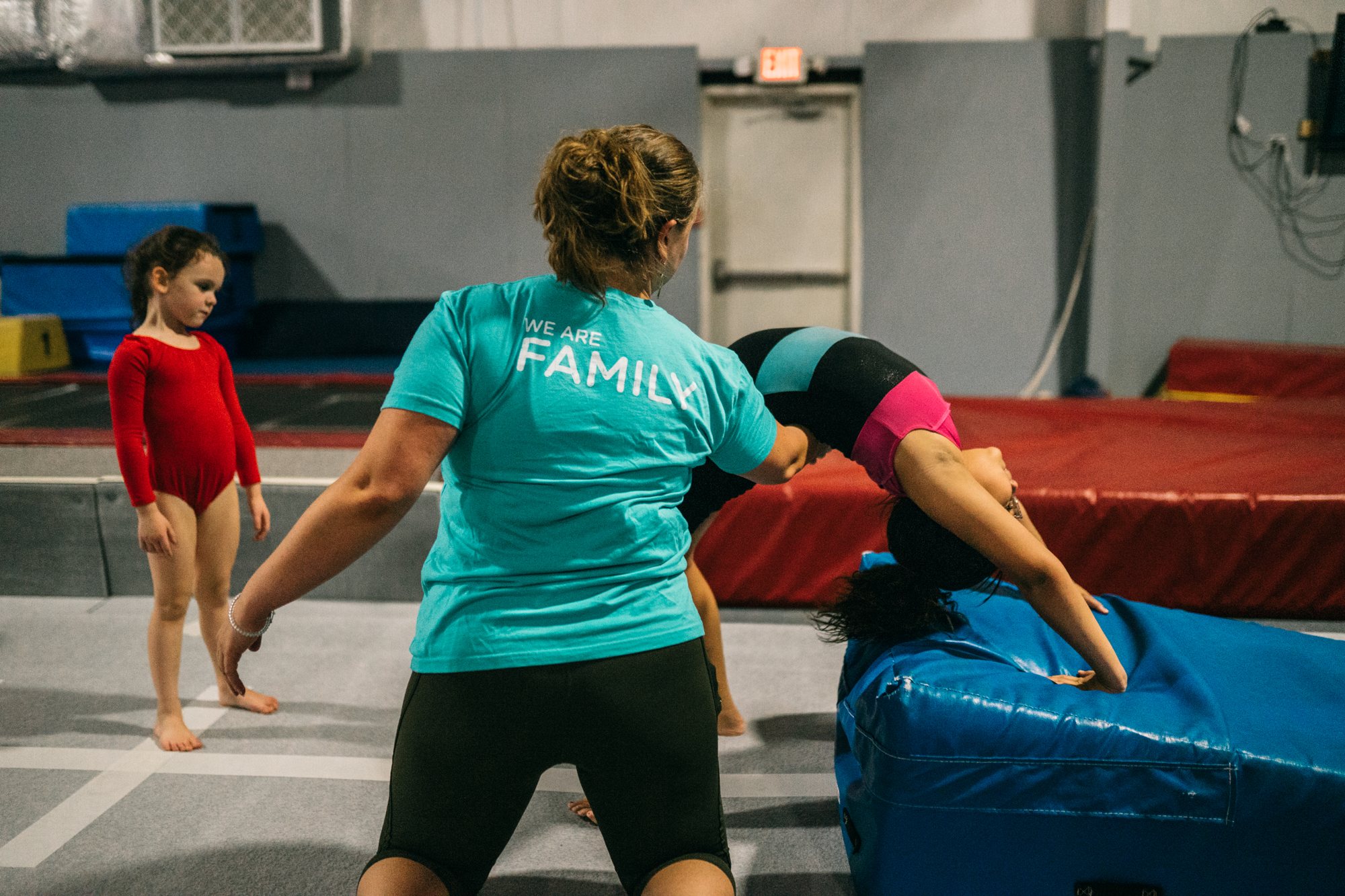 A Gym Counts coach guiding a young gymnast through a skill