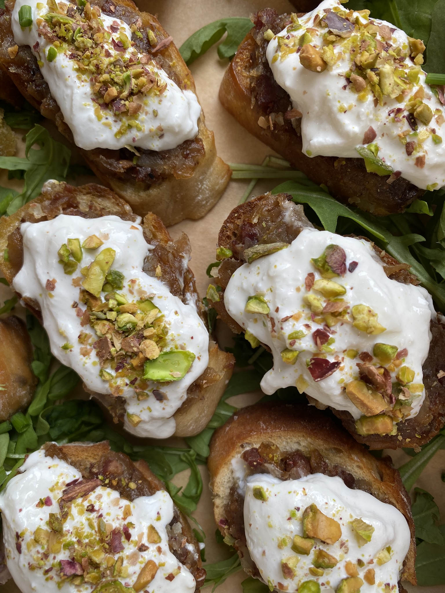 Handmade canapé crostini with whipped ricotta, caramelized onions and crushed pistachios by crumbelle