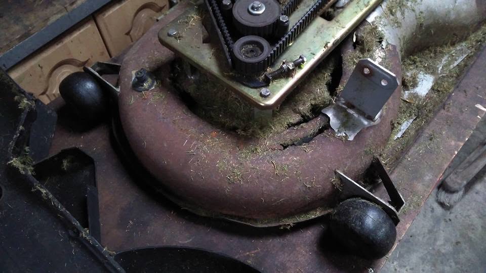 Rotted and cracked mower cutting deck with pulley drive assembly inspected on the workshop bench at RM Lawnmowers, Meath
