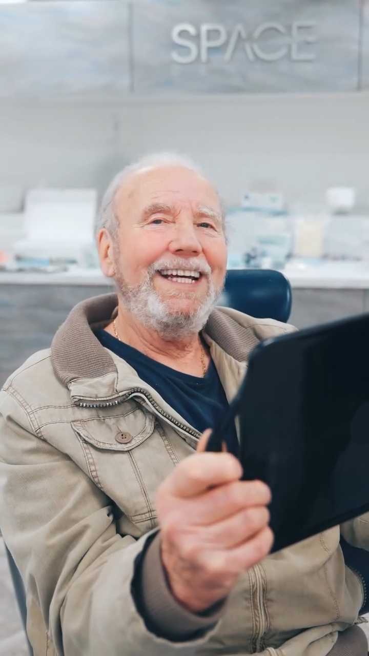 Smiling happy patient holding mirror at Space Dental