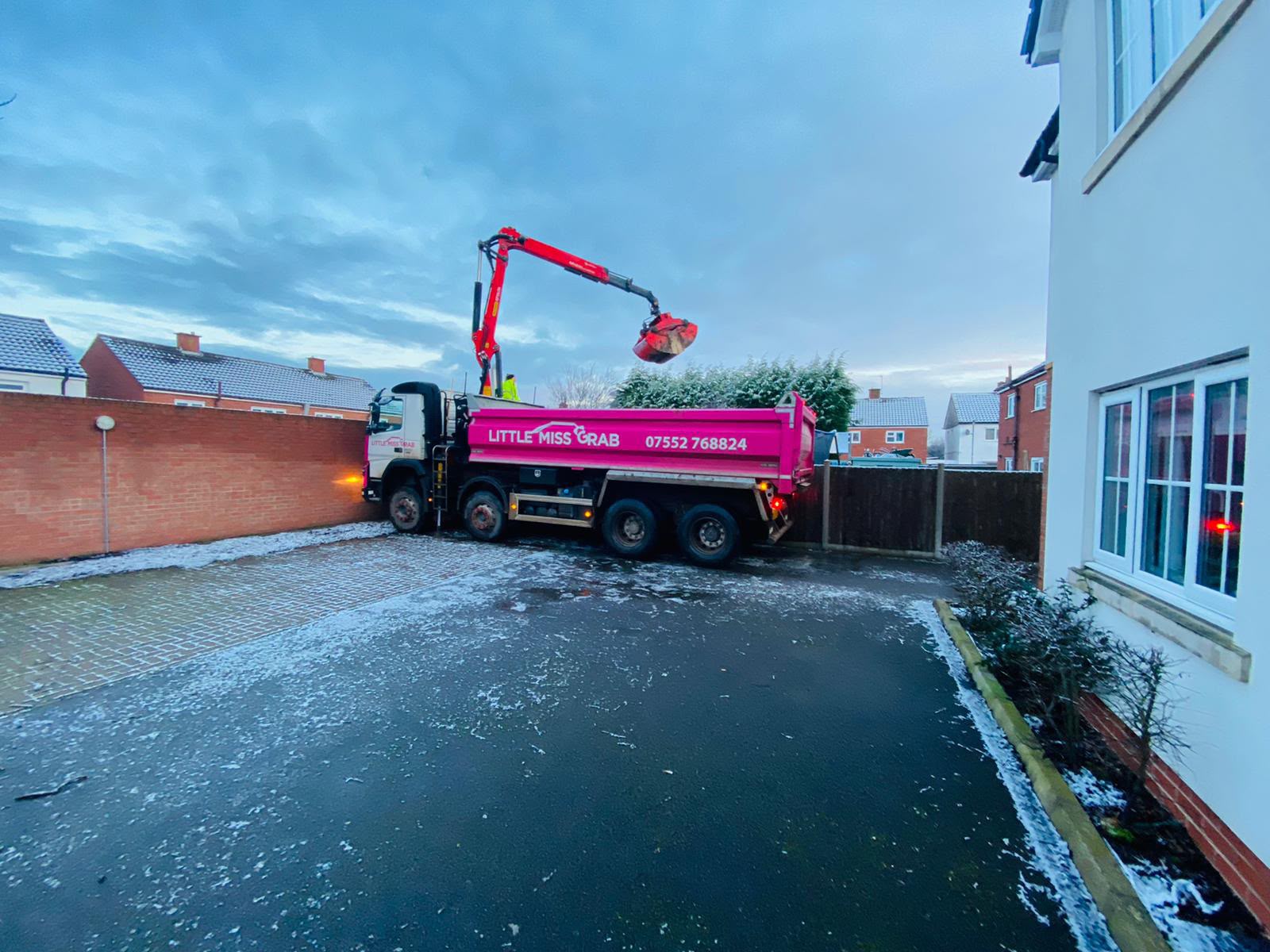 Little Miss Grab lorry extending hydraulic arm over residential fence in winter weather